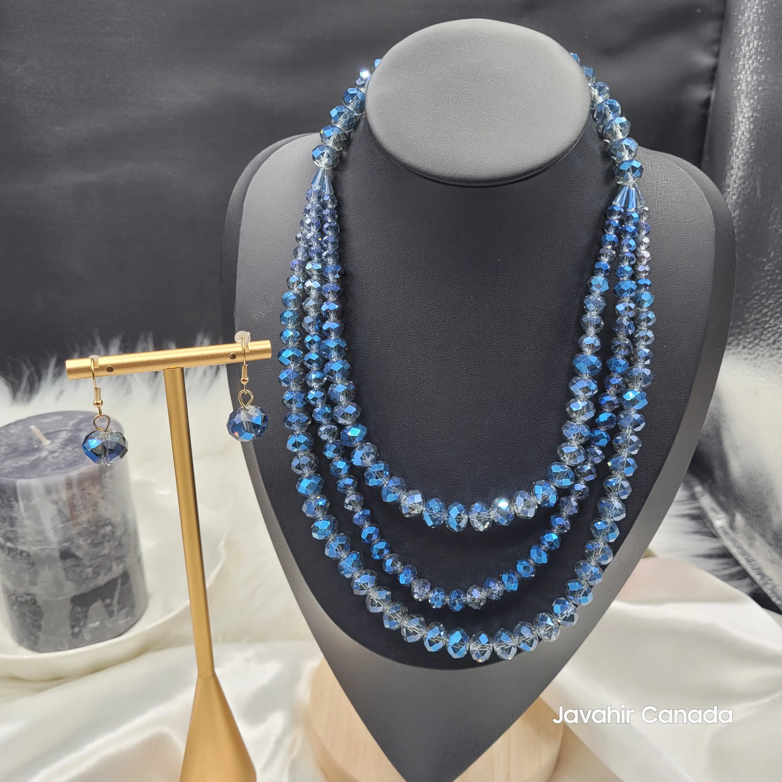 JV162 necklace set in bold sapphire blue crystal beads fading into grey tones, layered in four strands and paired with matching earrings on a gold stand.
