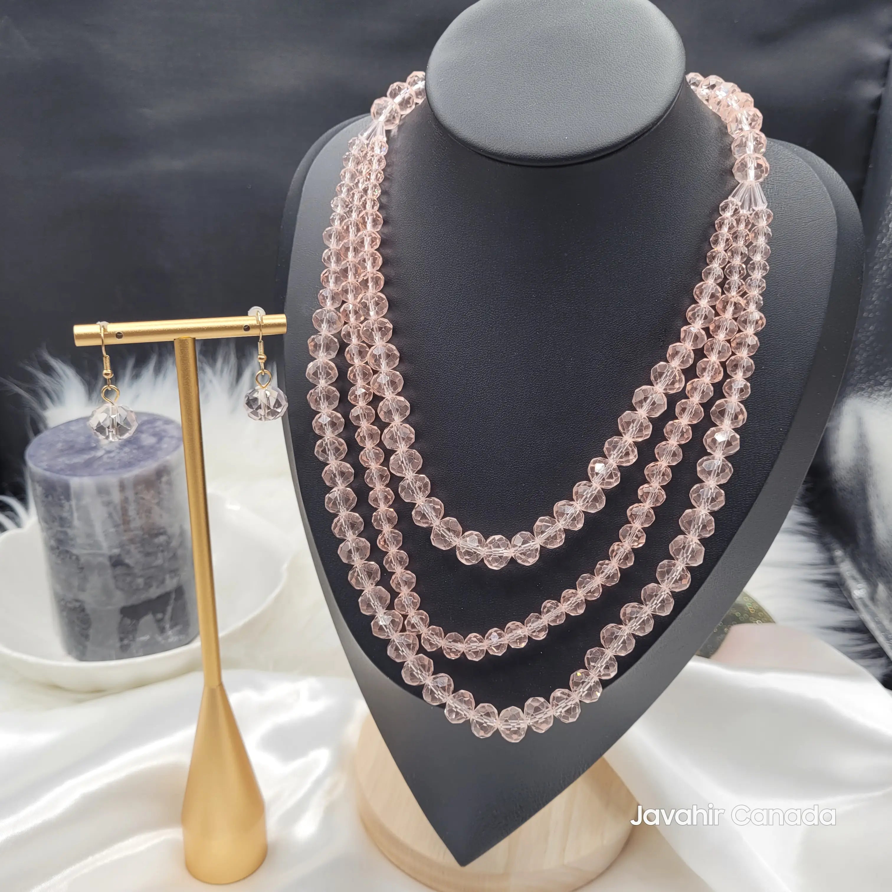 Front view of the JV162 necklace set in elegant rose pink faceted glass beads, featuring four graduated strands and matching earrings, presented on a black bust and gold stand.