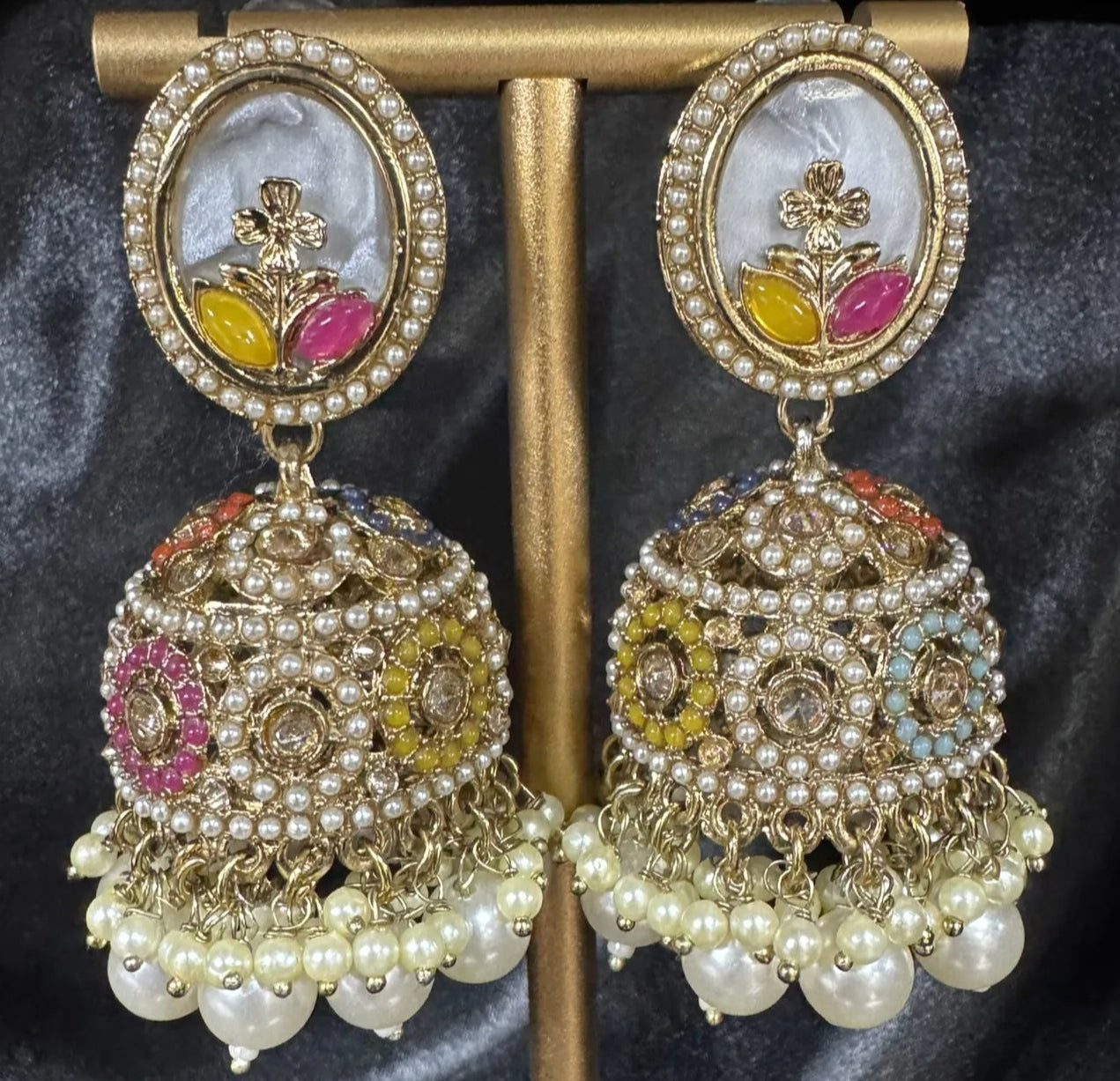 Ornate earrings on a gold stand against a dark fabric background