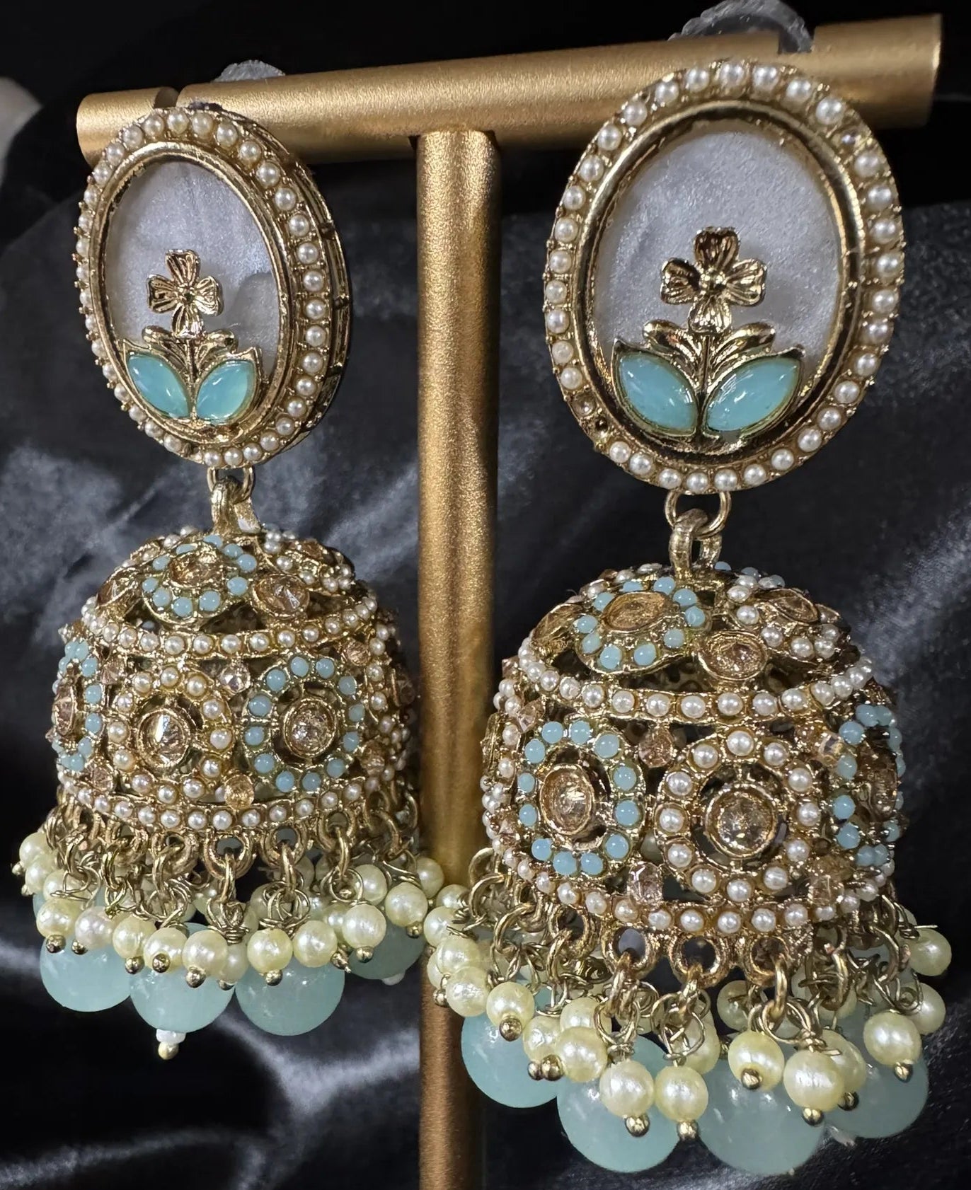 Ornate earrings with gold and blue details on a black satin background