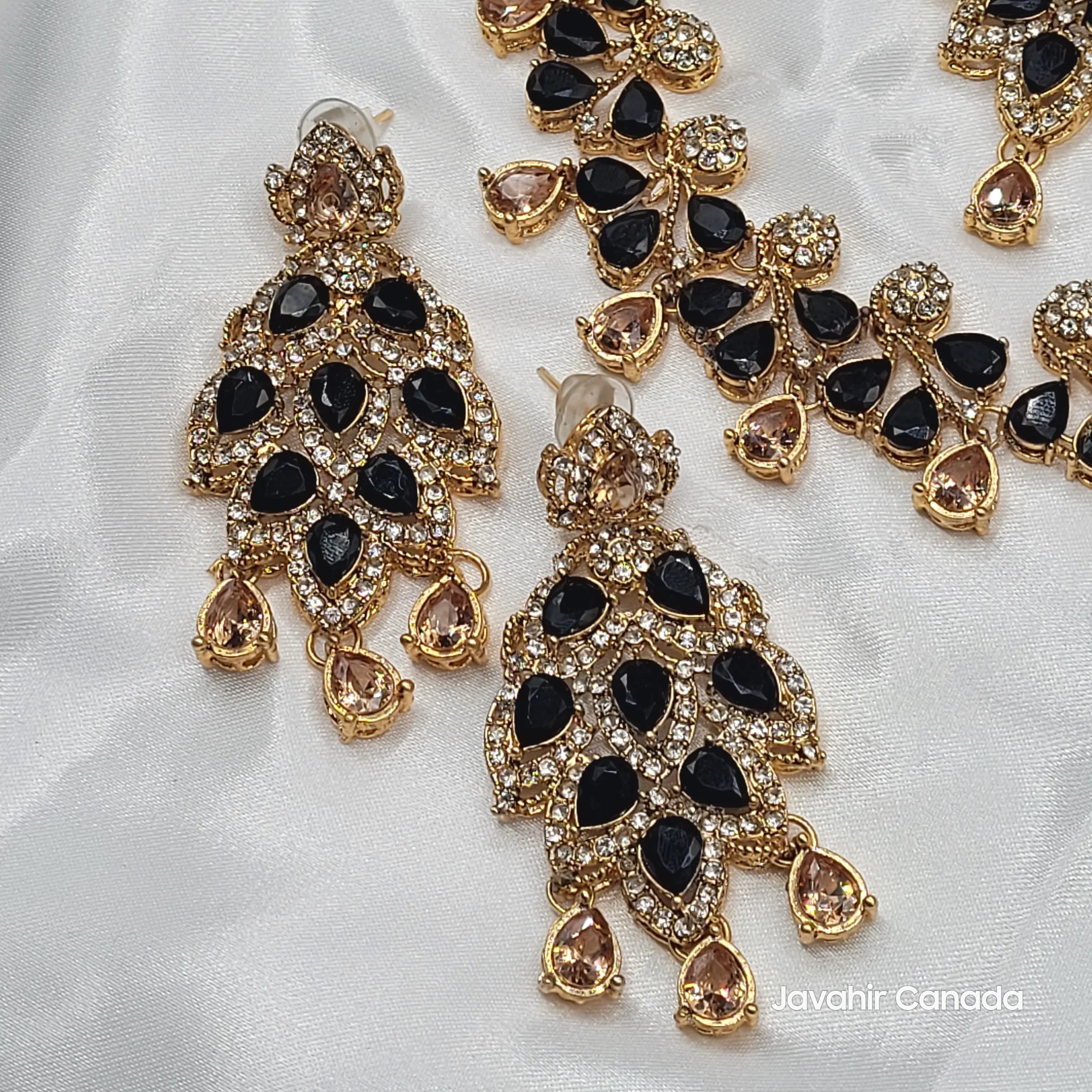 Close-up of JV20 black earrings with teardrop CZ and gold setting on white satin