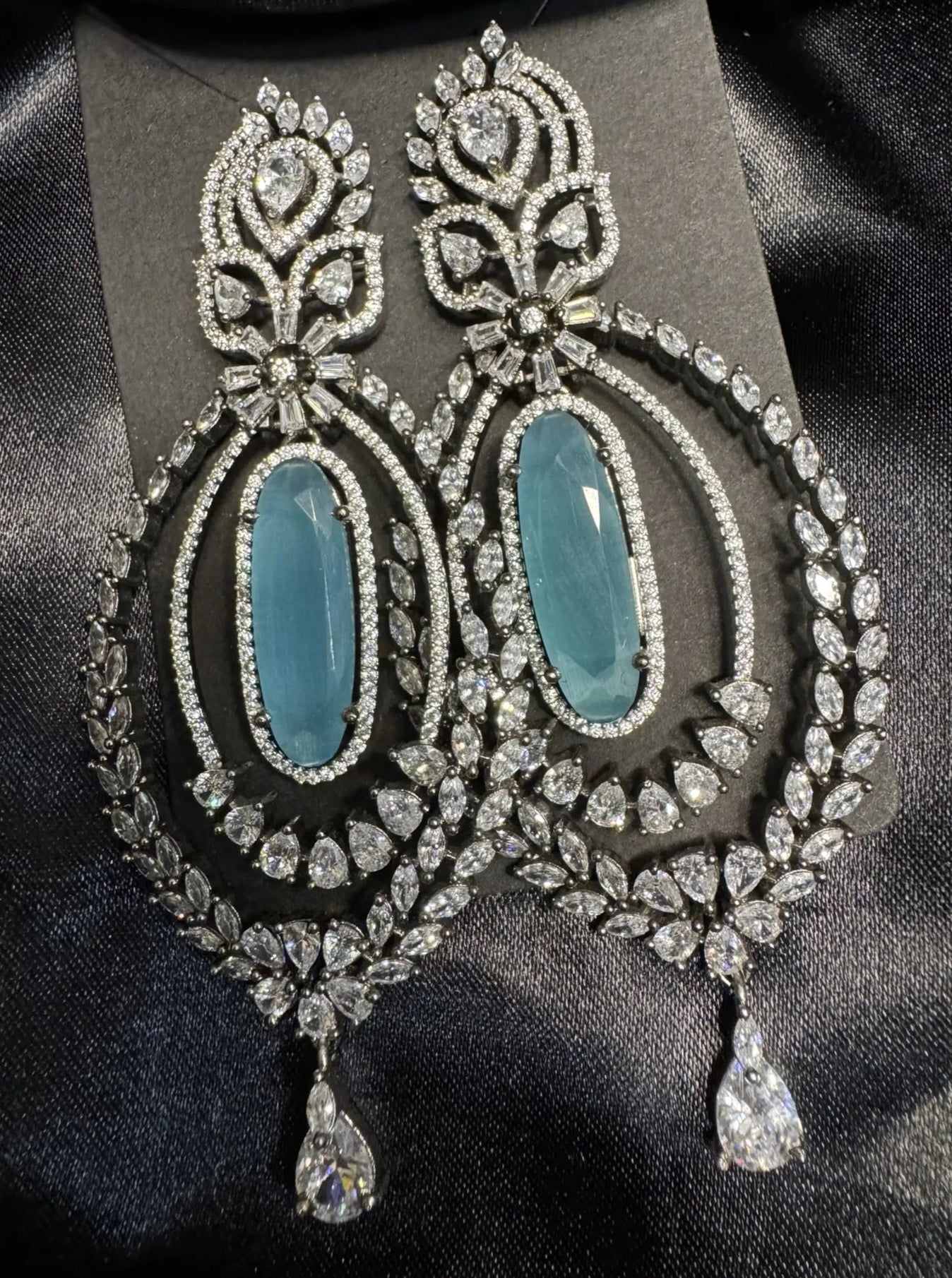 Ornate earrings with turquoise stones and American diamond accents on a black background