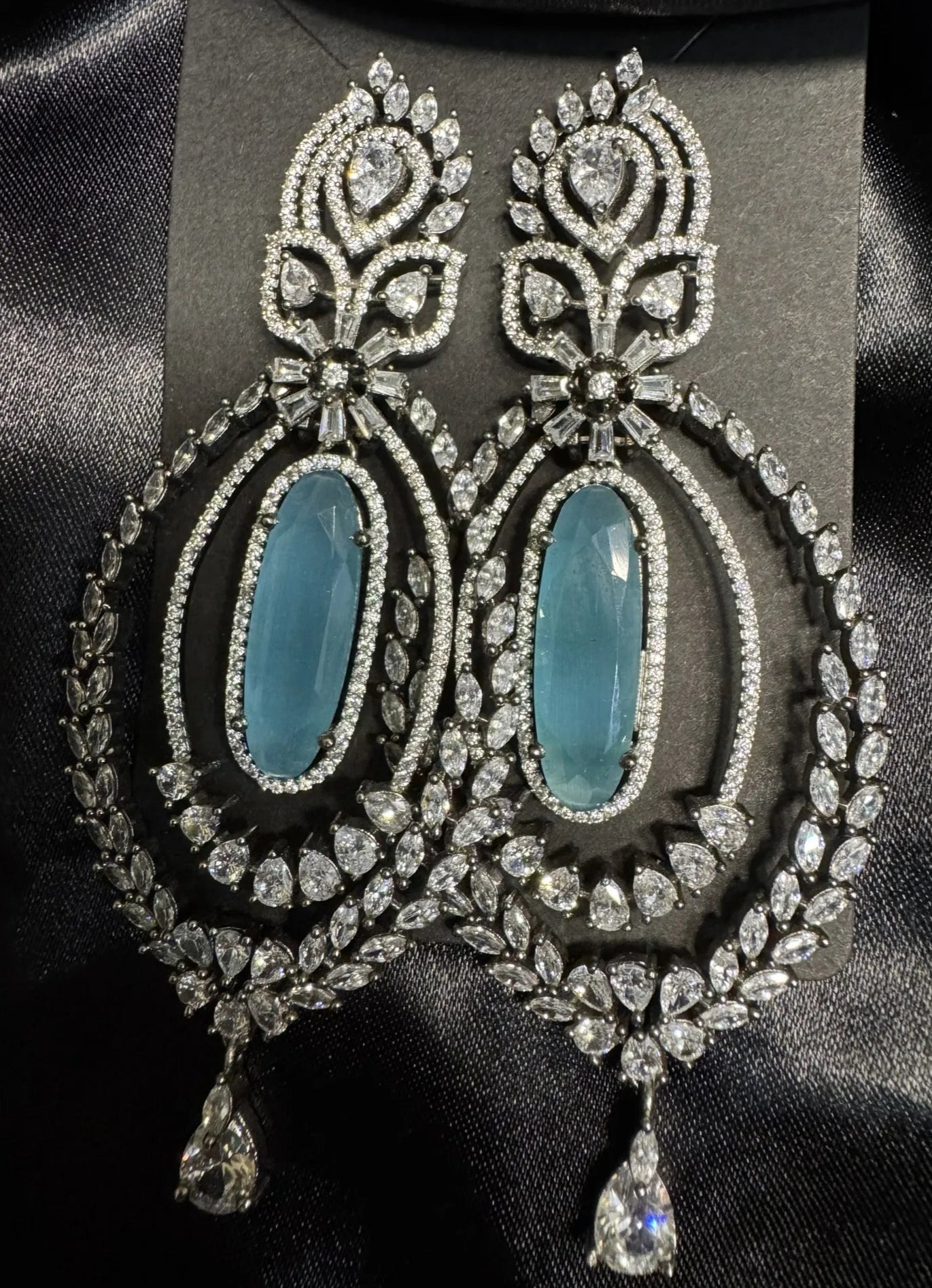 Ornate earrings with turquoise stones and American diamond accents on a black background and silk cloth