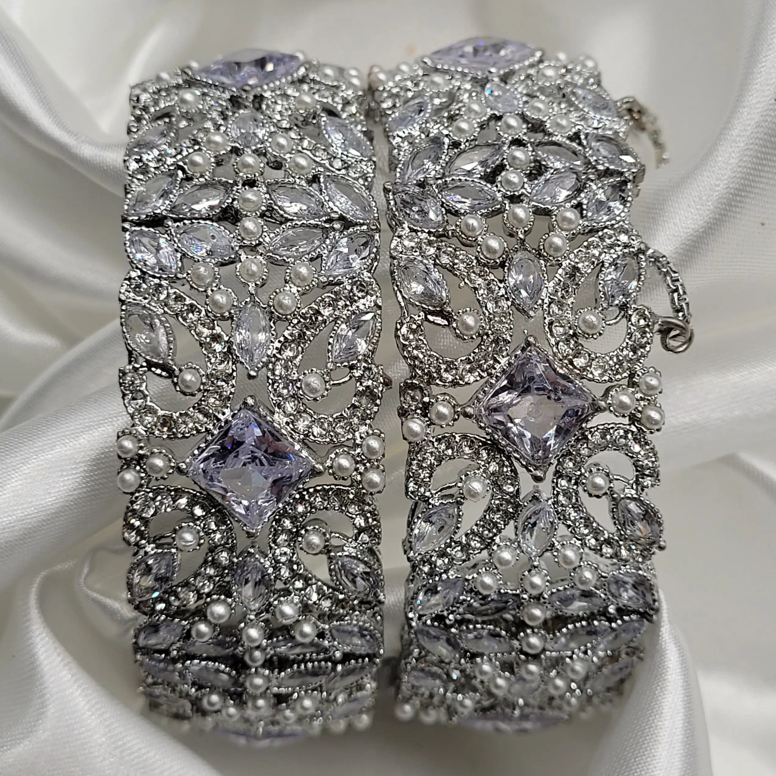 Silver jewelry bangles with gemstones on a white satin background