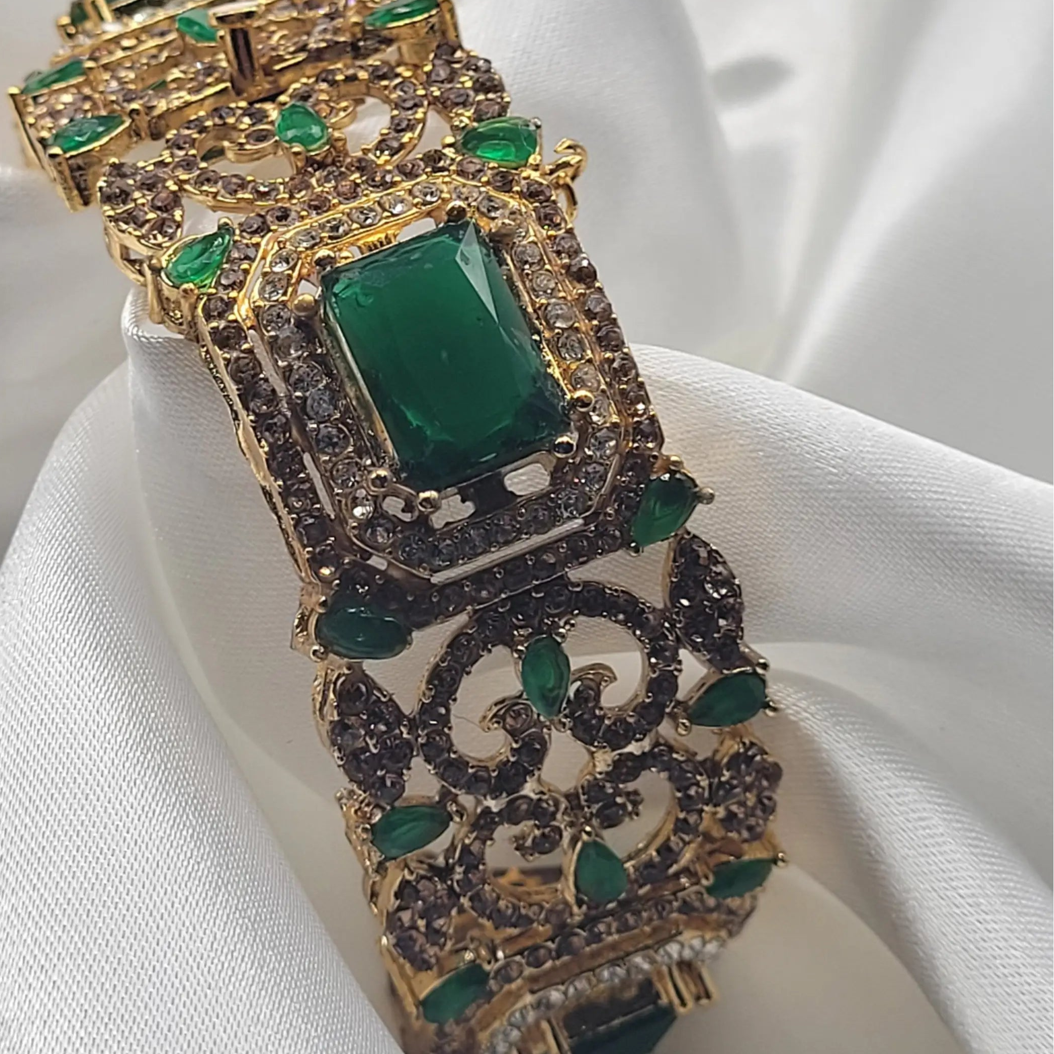 openable Bangle with green gemstones and gold accents on a white fabric background