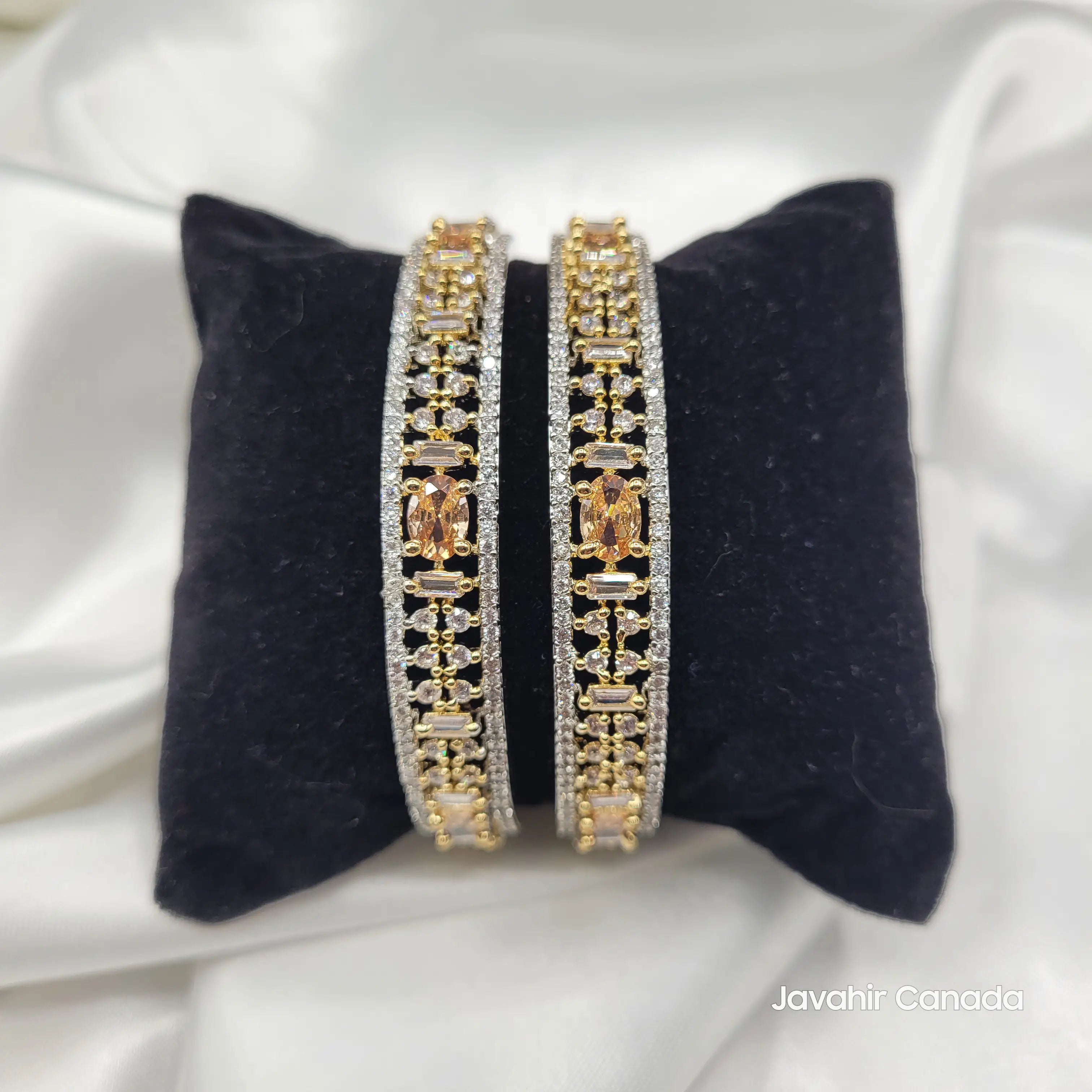 Pair of gold and silver bangles on a black cushion with a white background