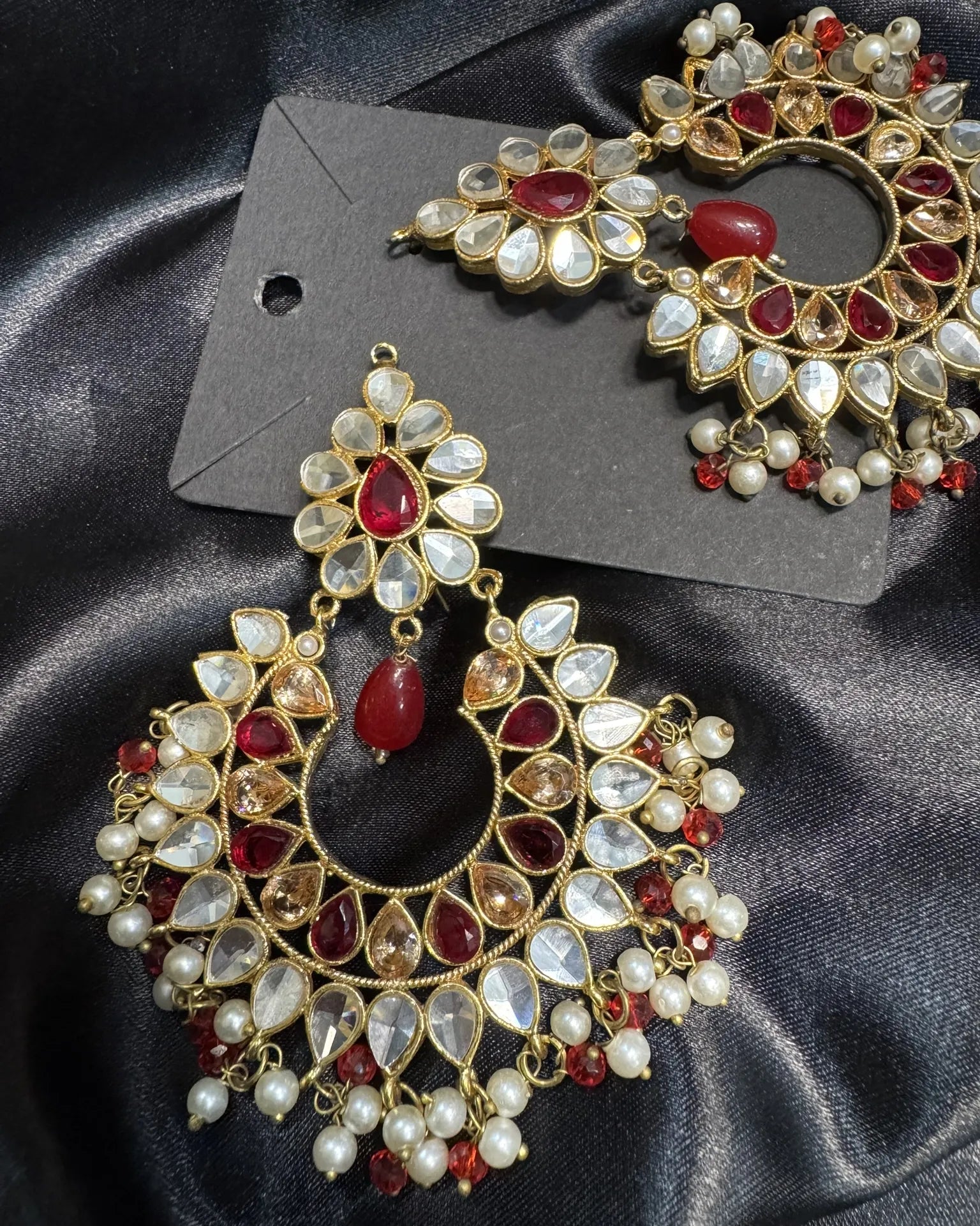 Ornate earrings with red and white stones on a dark fabric background