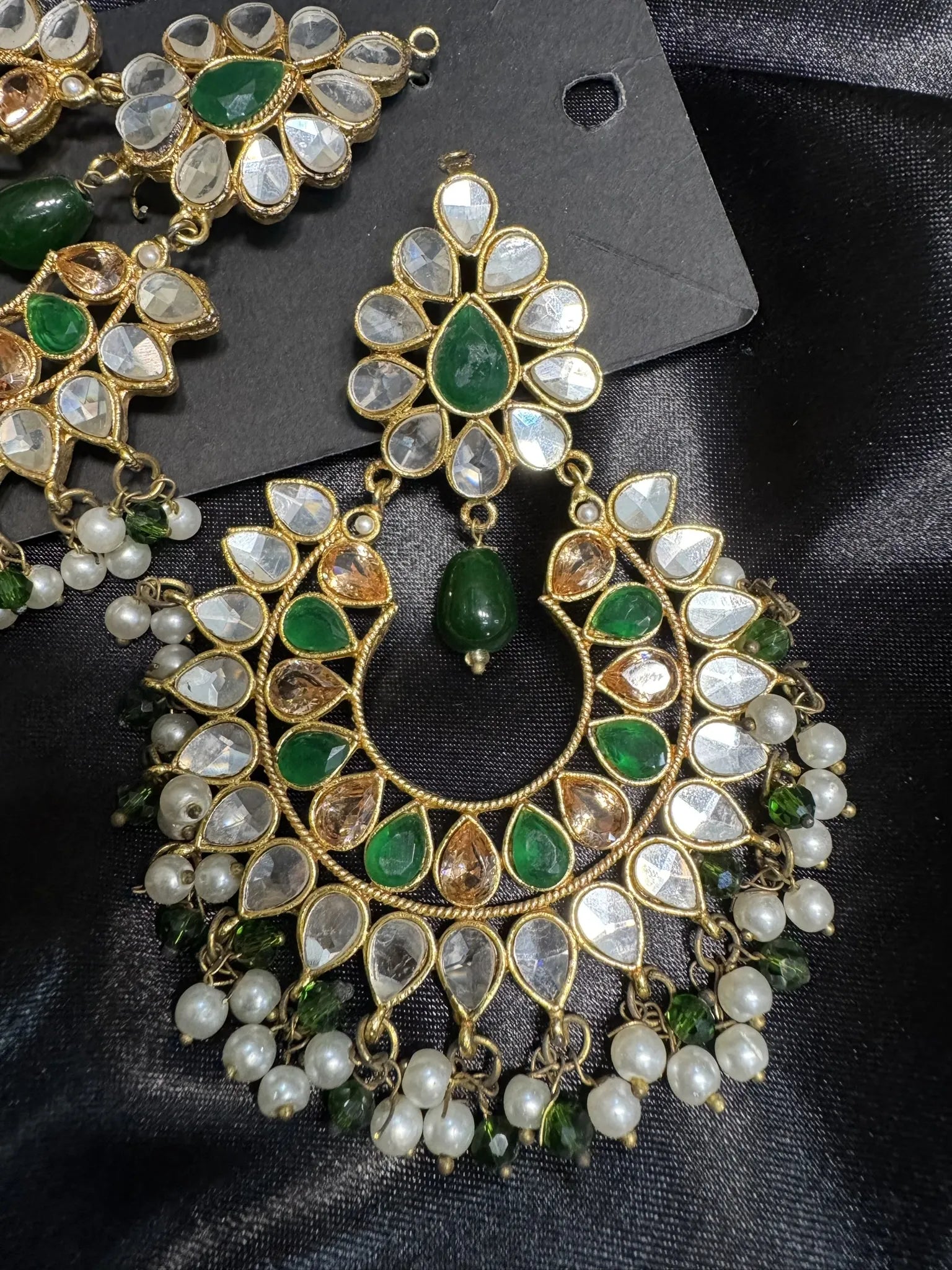 Ornate earrings with green and white gemstones on a black background