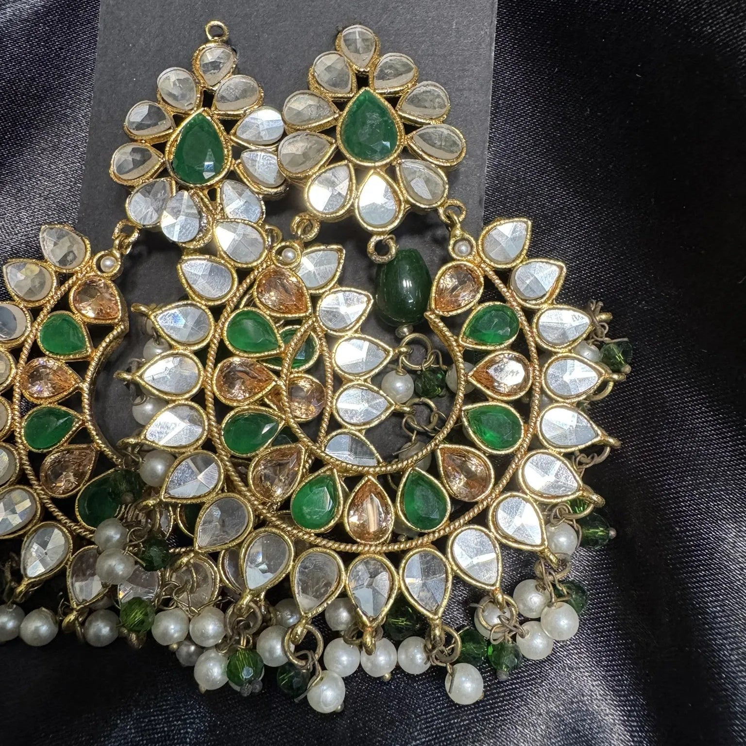 Ornate earrings with green and white gemstones on a dark fabric background