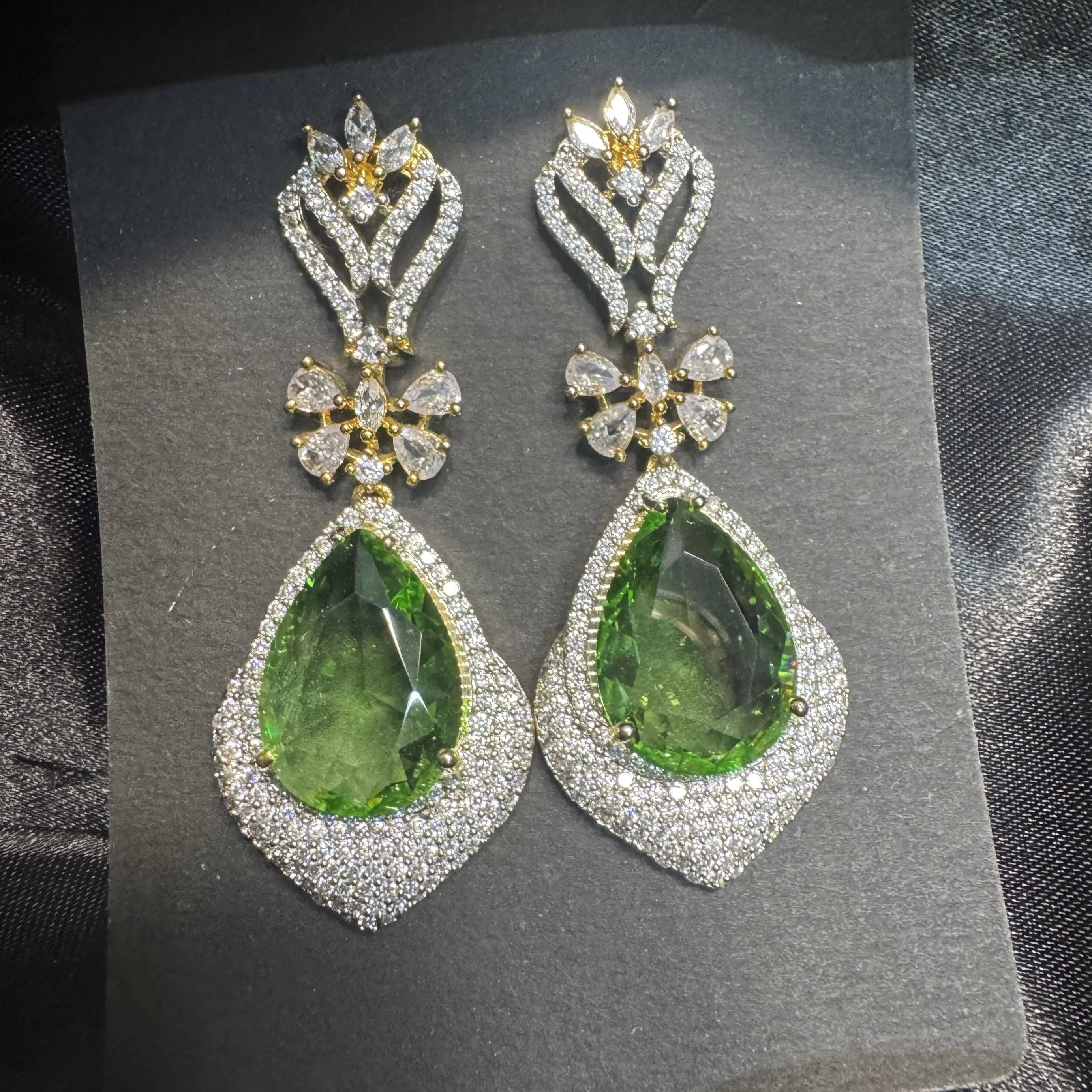 Pair of green teardrop earrings with American diamonds stones on a dark background