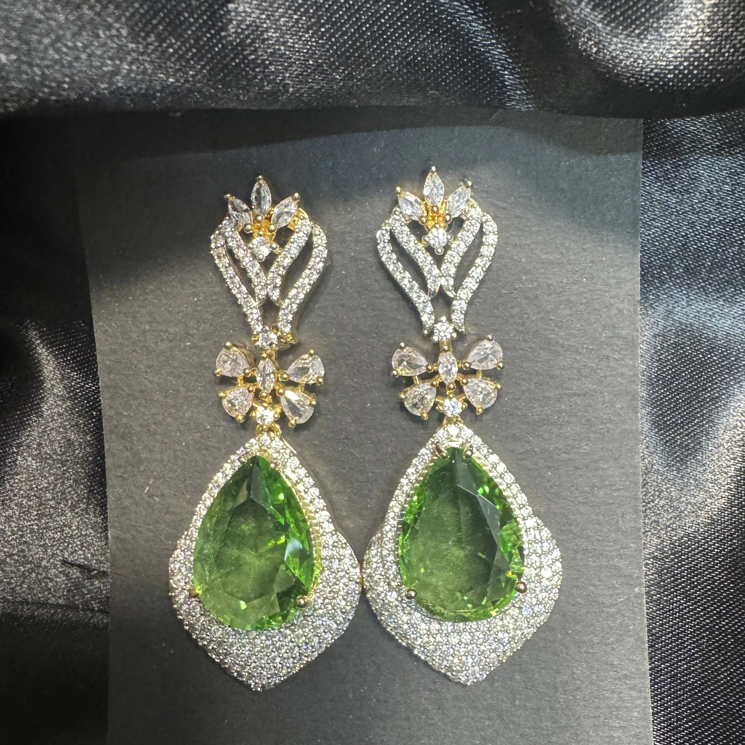 Pair of green teardrop earrings with gold and American diamonds accents on a dark gray card.