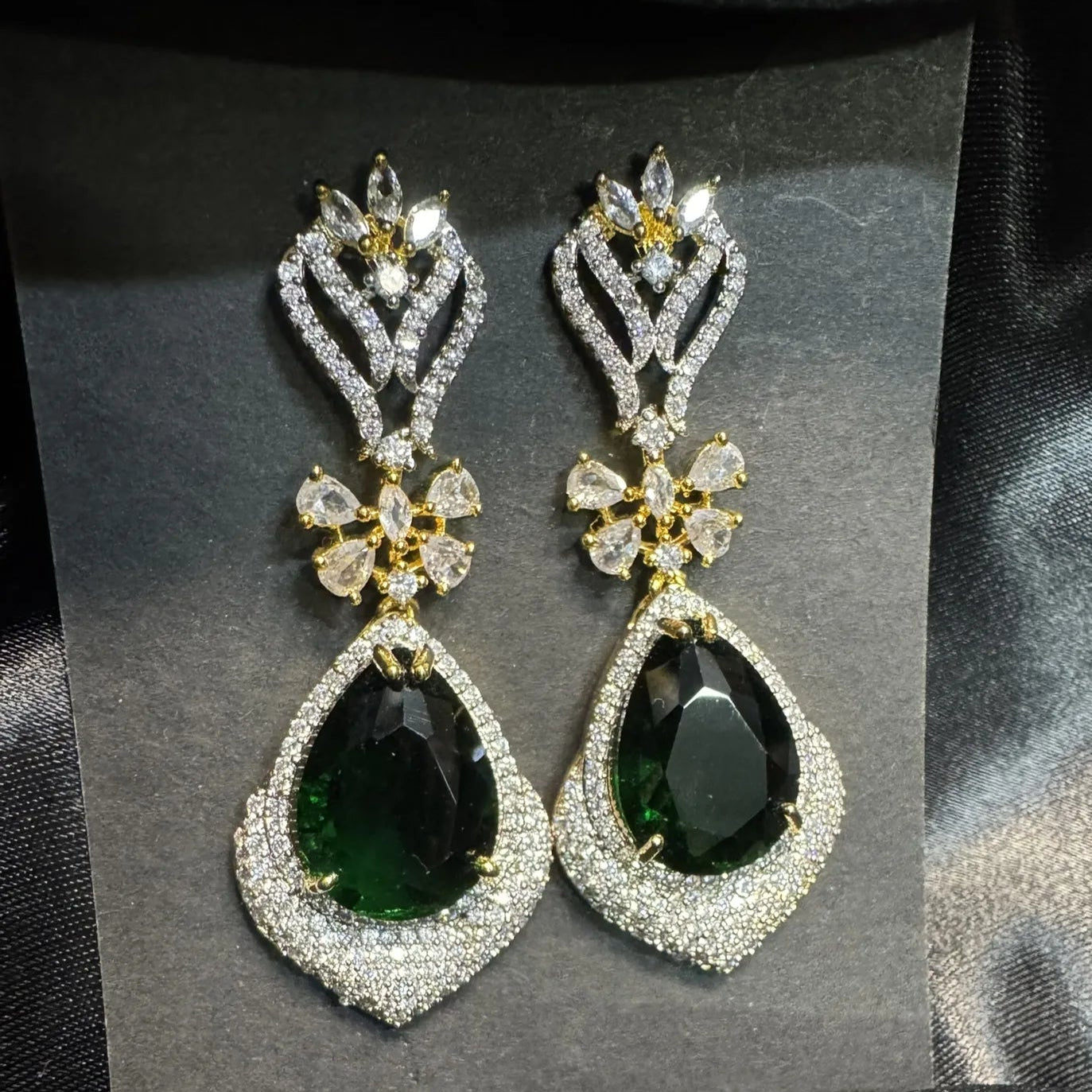 Pair of earrings with American diamonds and  emerald gemstones on a gray card