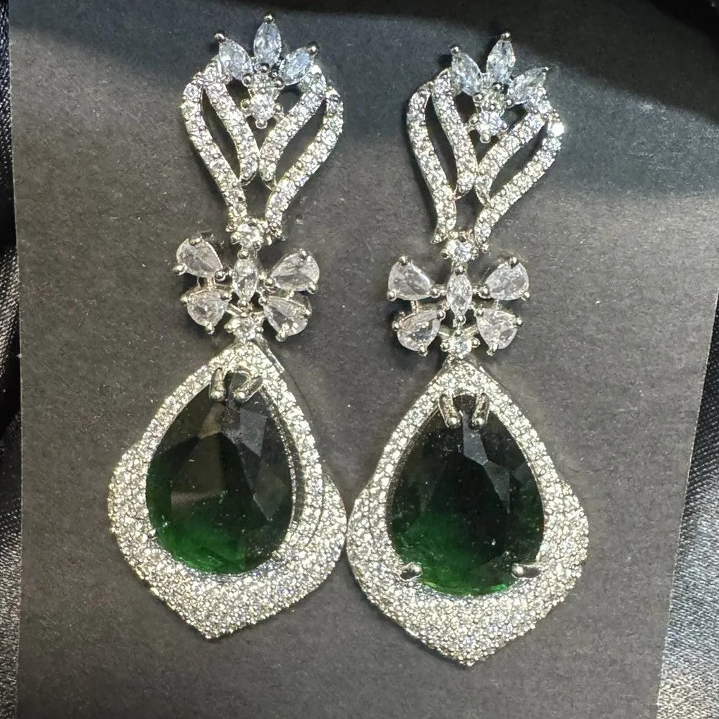 Pair of earrings with green gemstones and American diamonds stones on a dark background