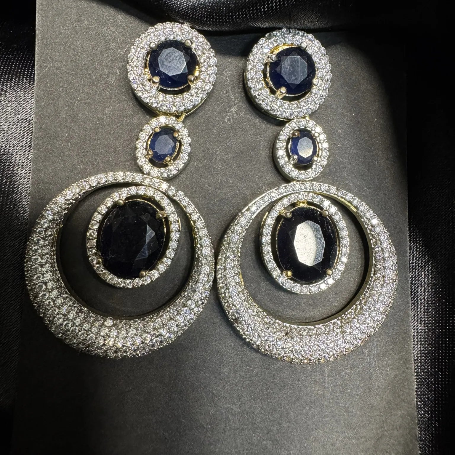 Pair of earrings with black gemstones and American diamonds  on a black fabric background