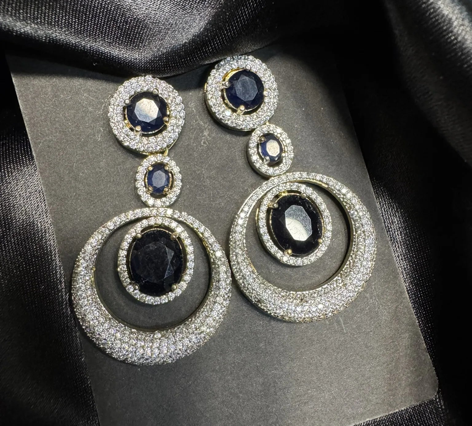top view of pair of earrings with black gemstones and American diamonds  on a black fabric background