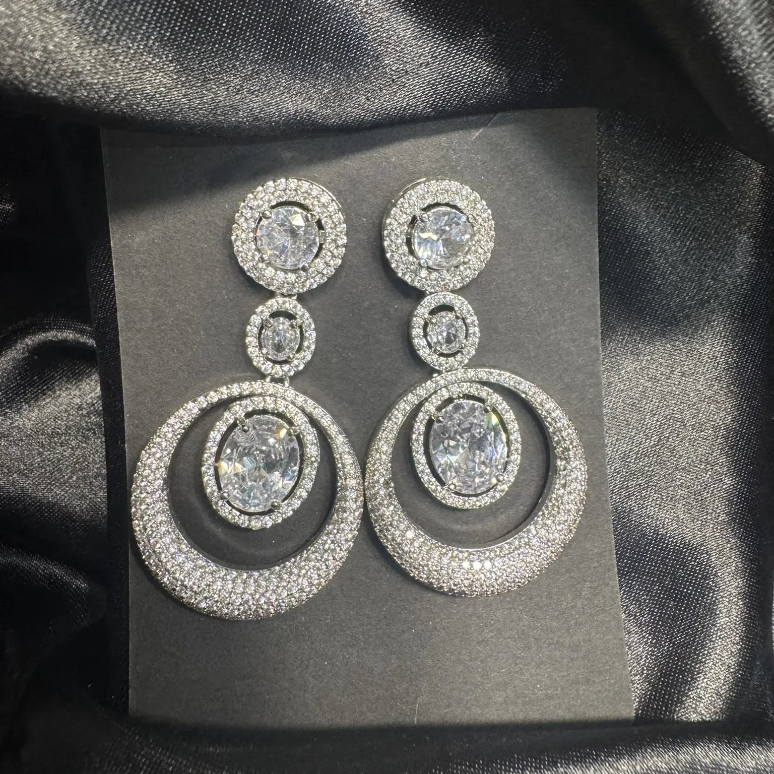 Pair of silver American diamonds earrings with multiple circular designs on a black satin background
