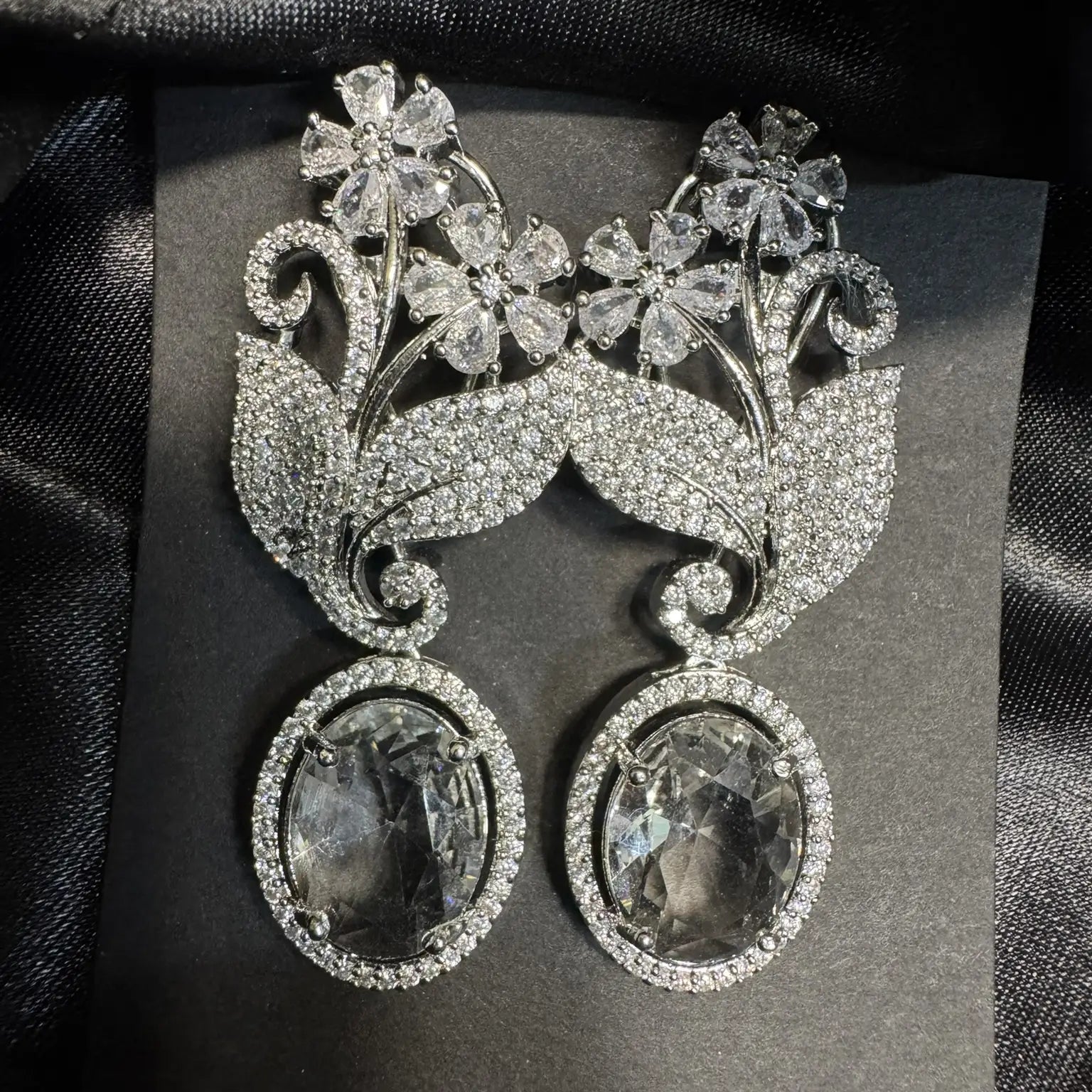Ornate silver earrings with gemstones and American diamonds on a dark background