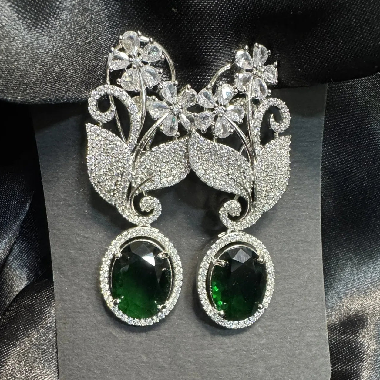 Pair of earrings with green gemstones on a gray card against a black satin background