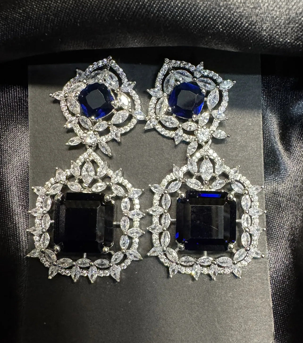 Pair of ornate earrings with blue gemstones on a black card