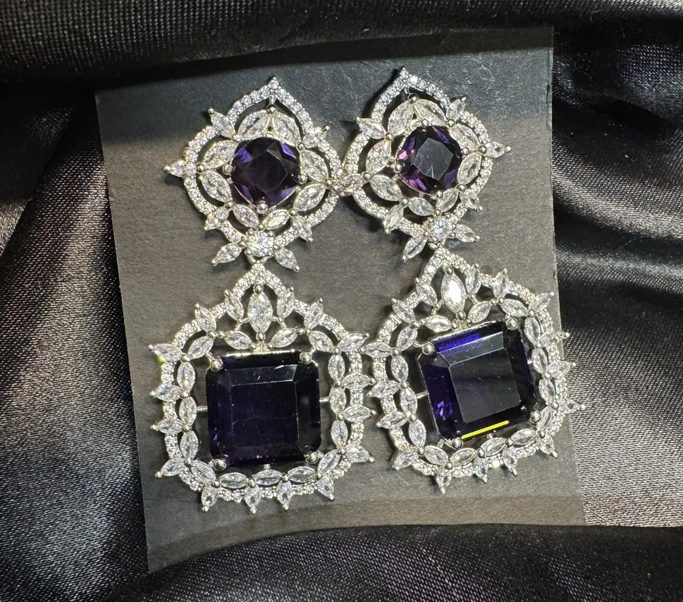 Pair of earrings with purple gemstones on a black satin background