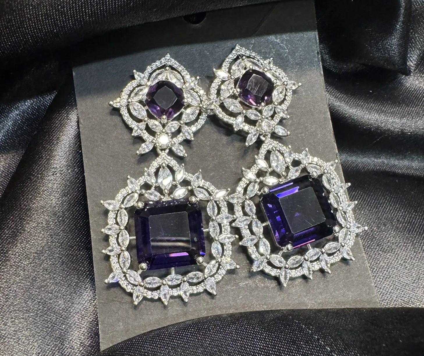 Pair of earrings with purple gemstones on a black card against a black fabric background