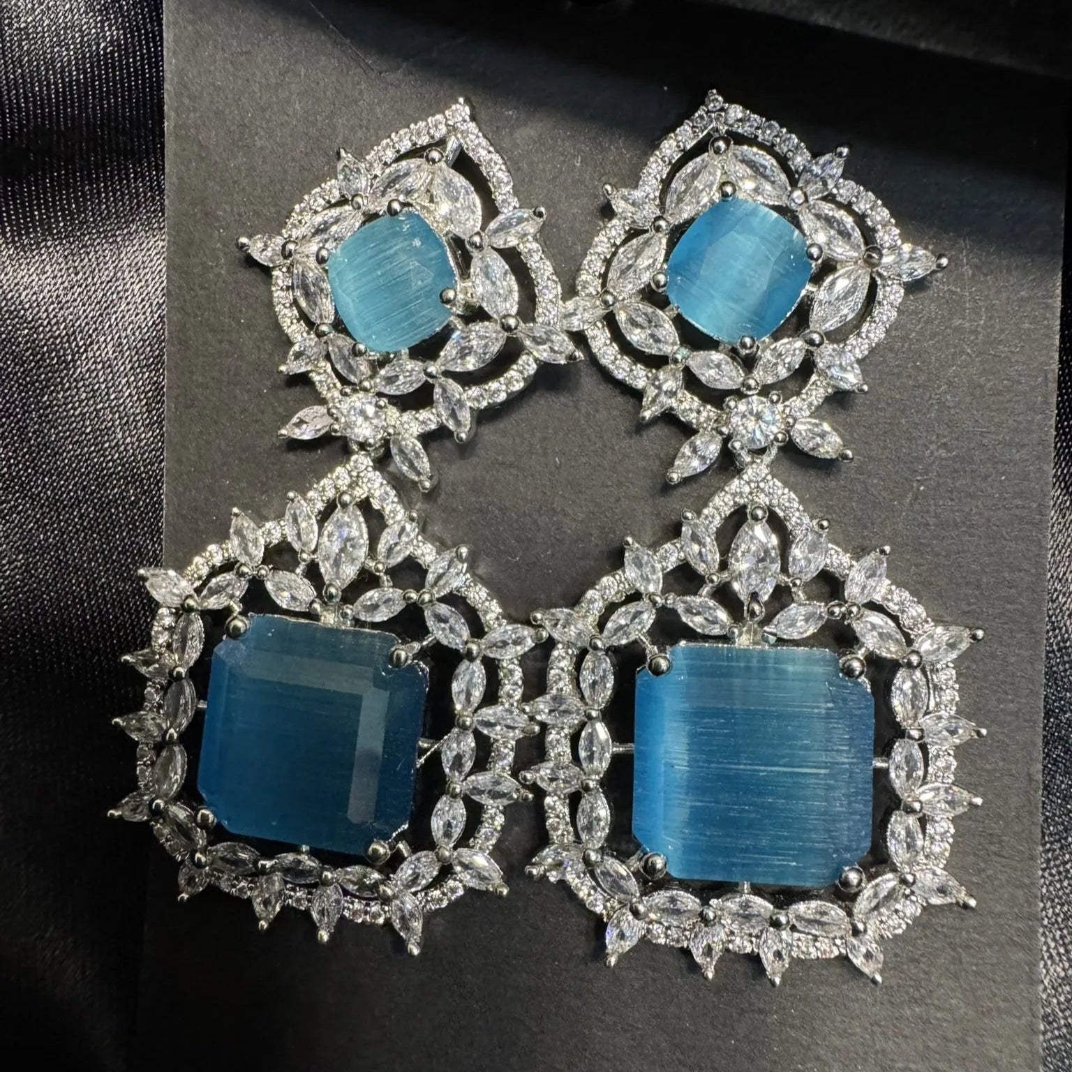 Pair of earrings with blue stones and silver or white gold frames on a black background