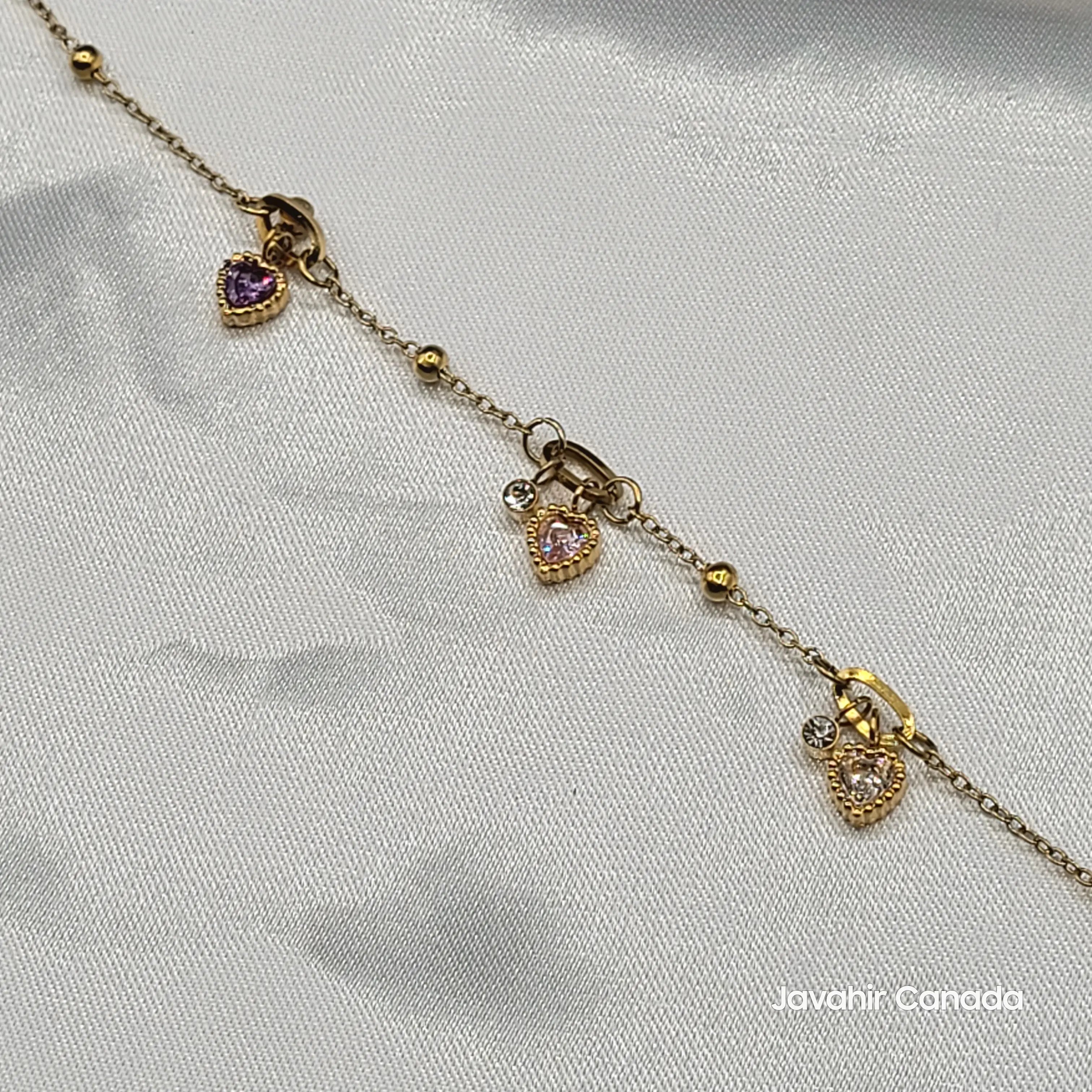 Close-up of gold-tone bracelet with pink, purple, and clear heart charms