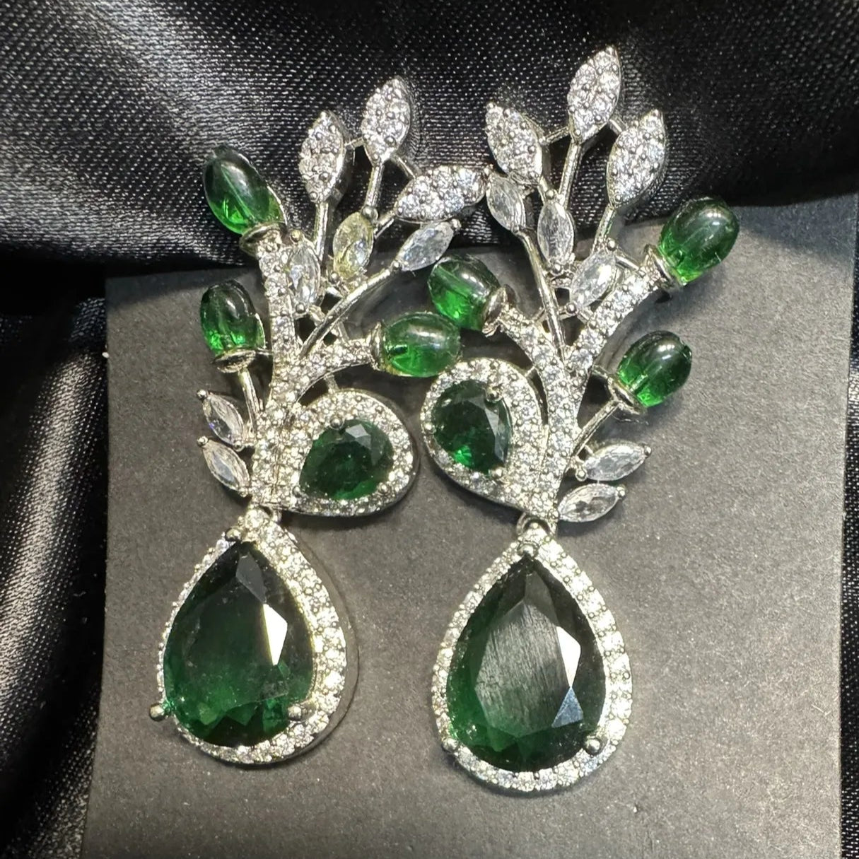 Pair of green gemstone earrings on a gray card with a black satin background