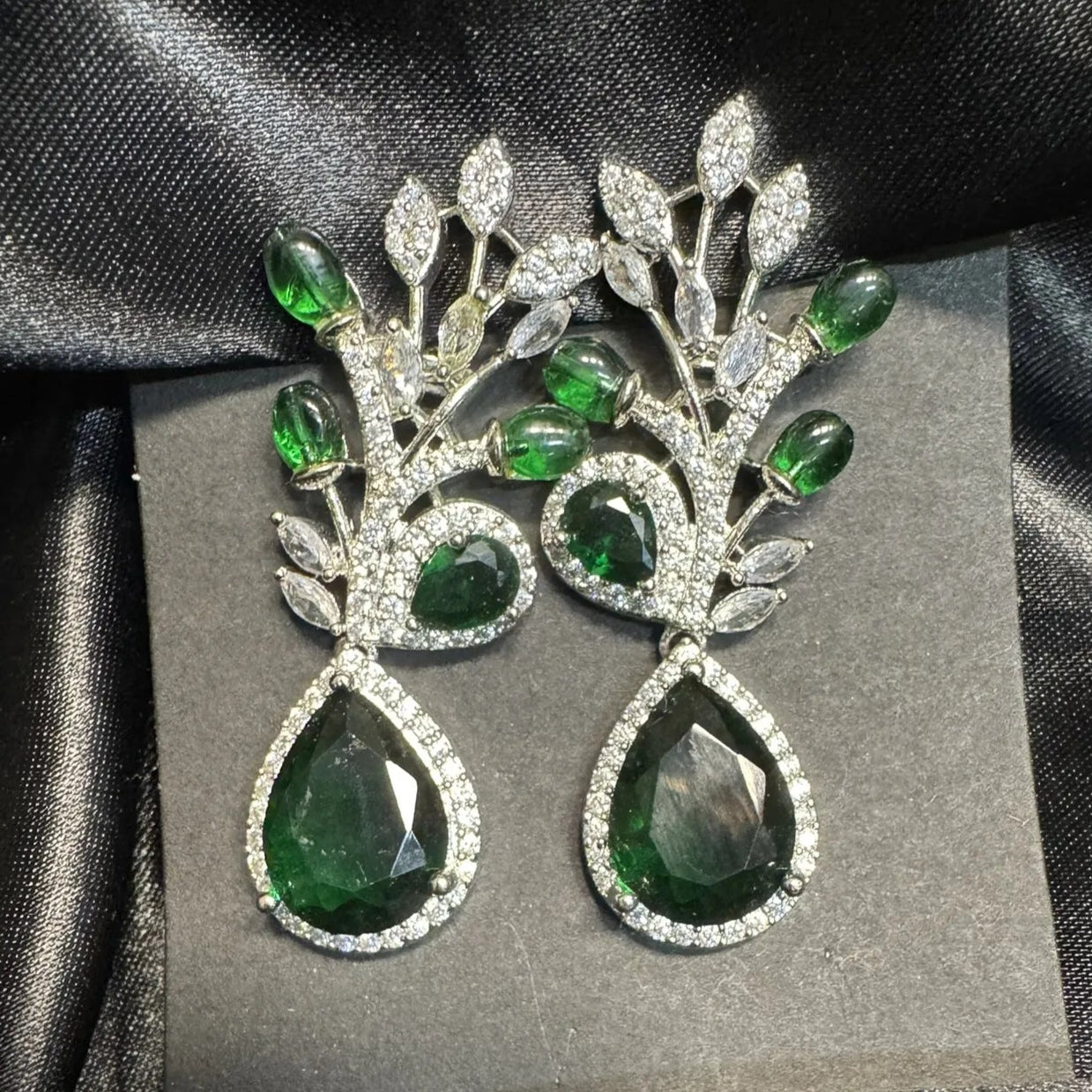 Pair of emerald and American diamond earrings on a black satin background