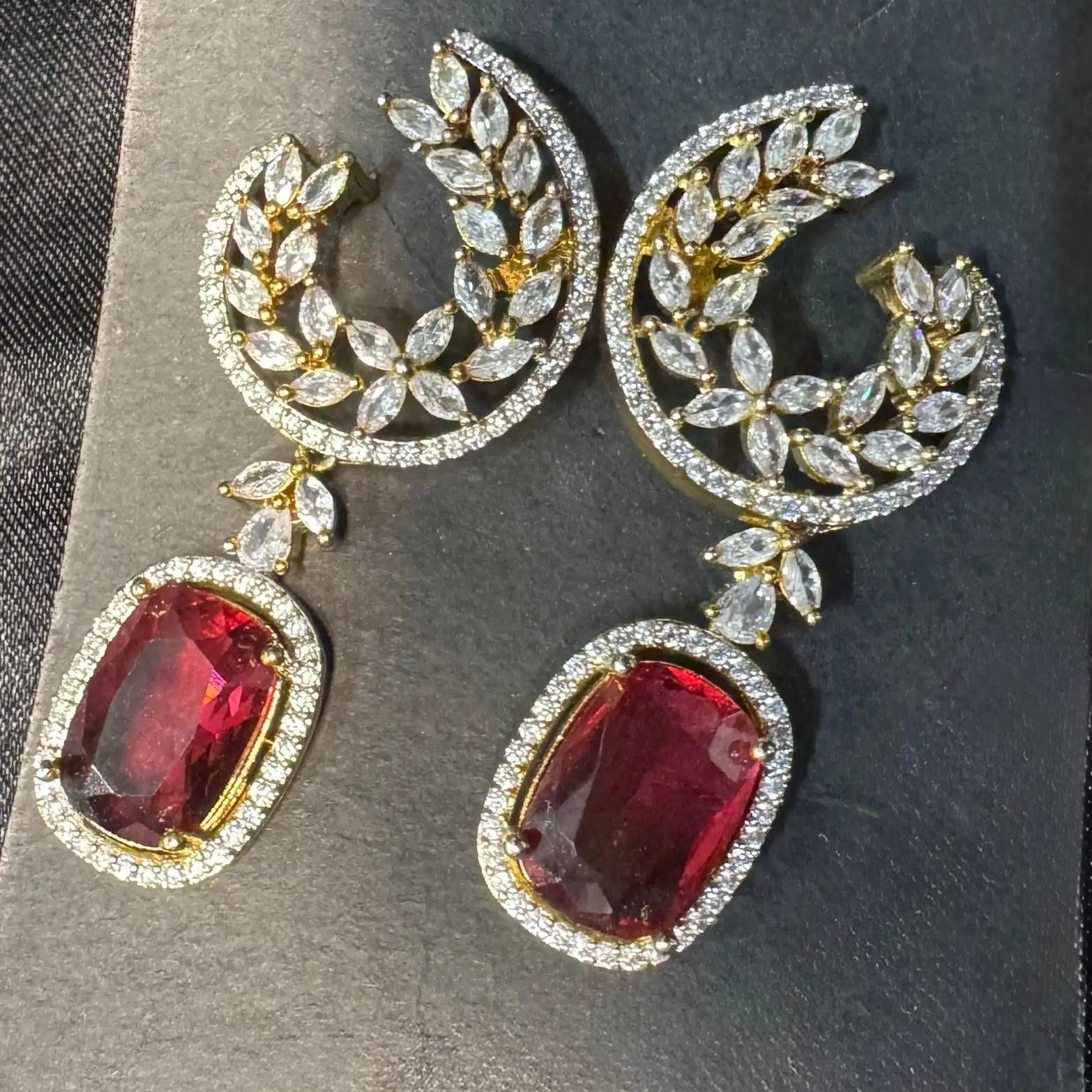 Pair of earrings with hotpink gemstones and gold accents on a dark background