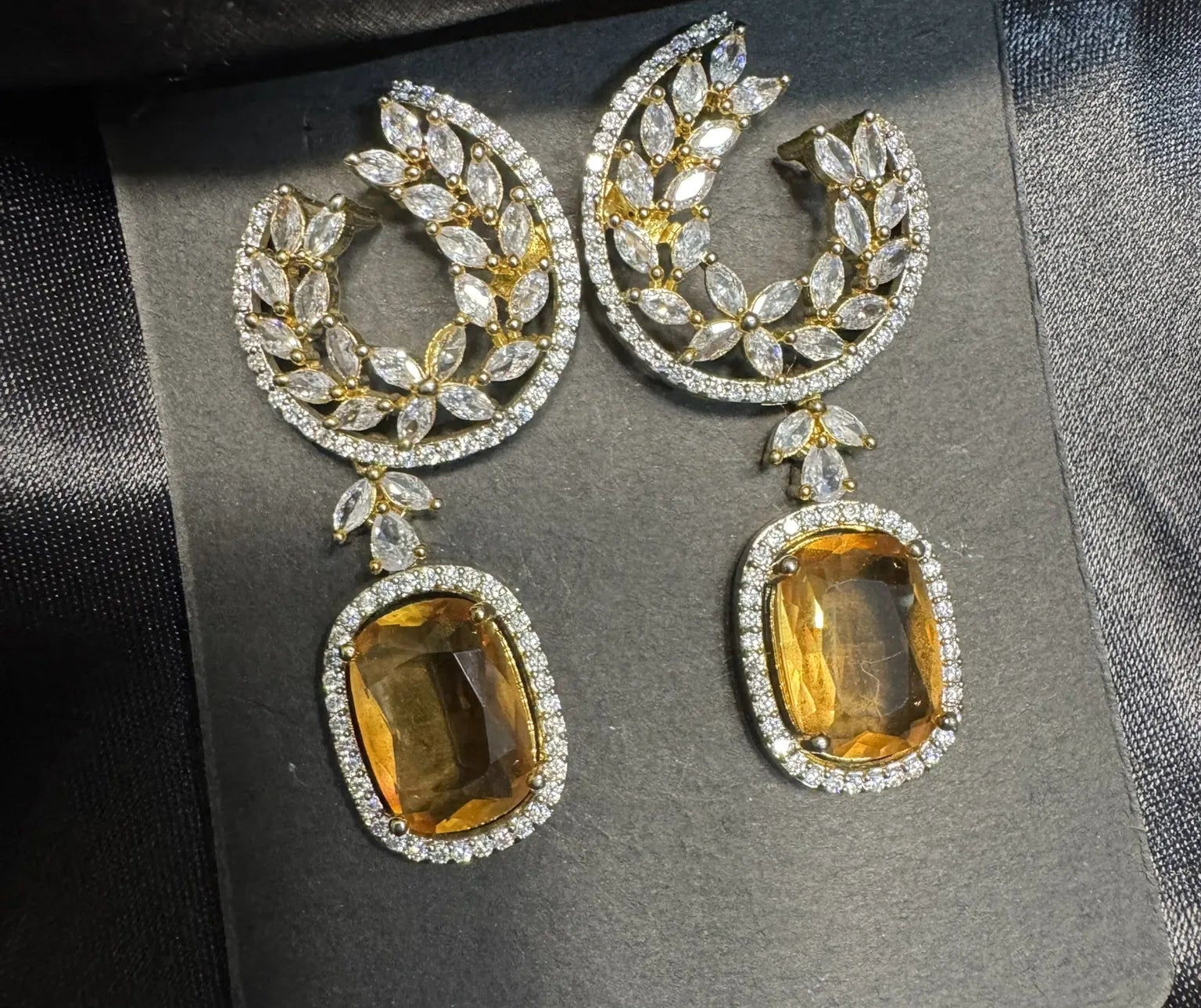 Pair of earrings with yellow gemstones and diamond-like stones on a gray card.