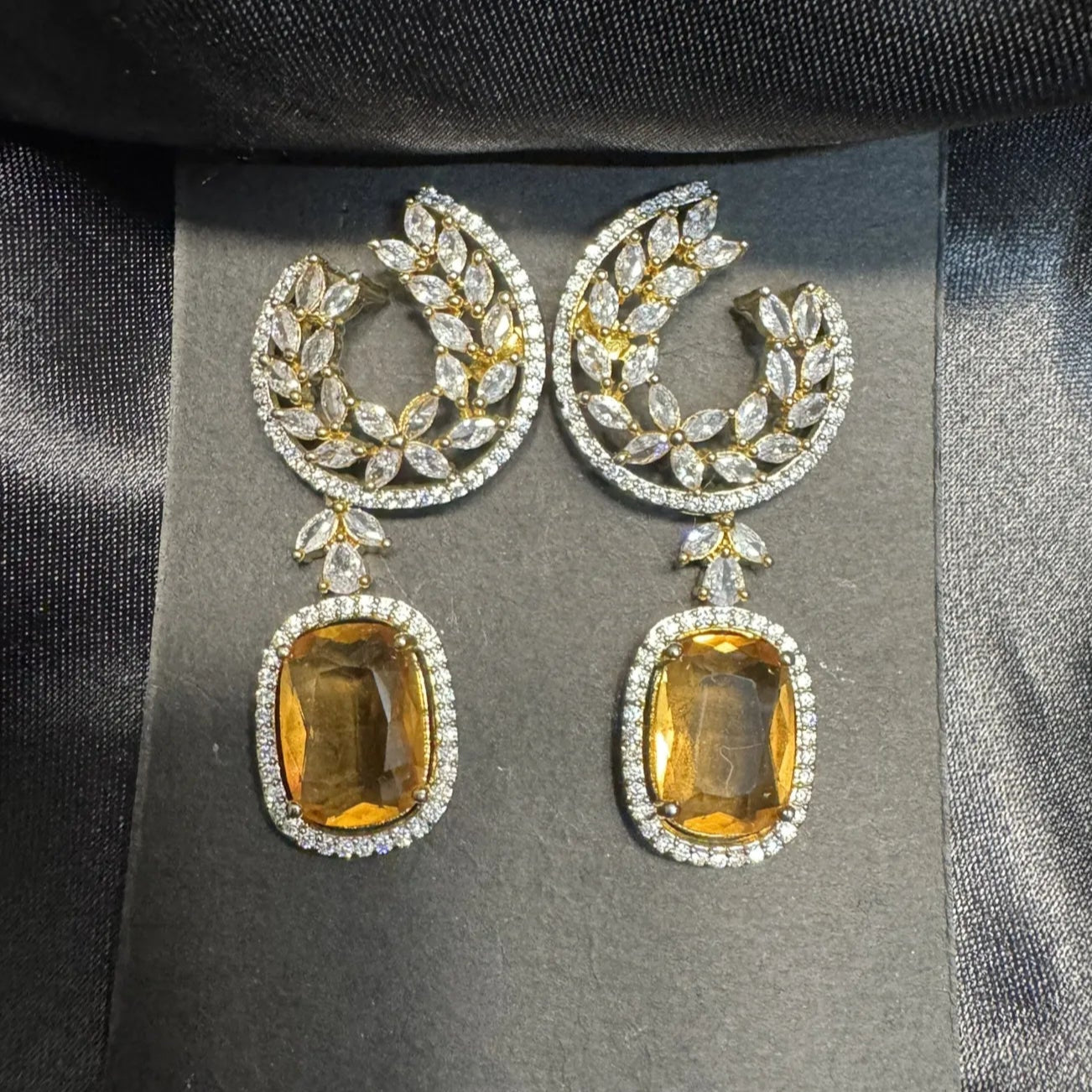 Pair of earrings with citrine stones on a gray card against a black satin background