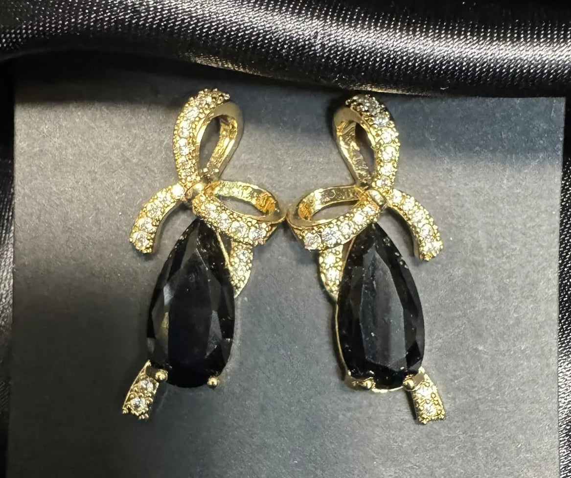 Pair of gold and black earrings on a dark fabric background