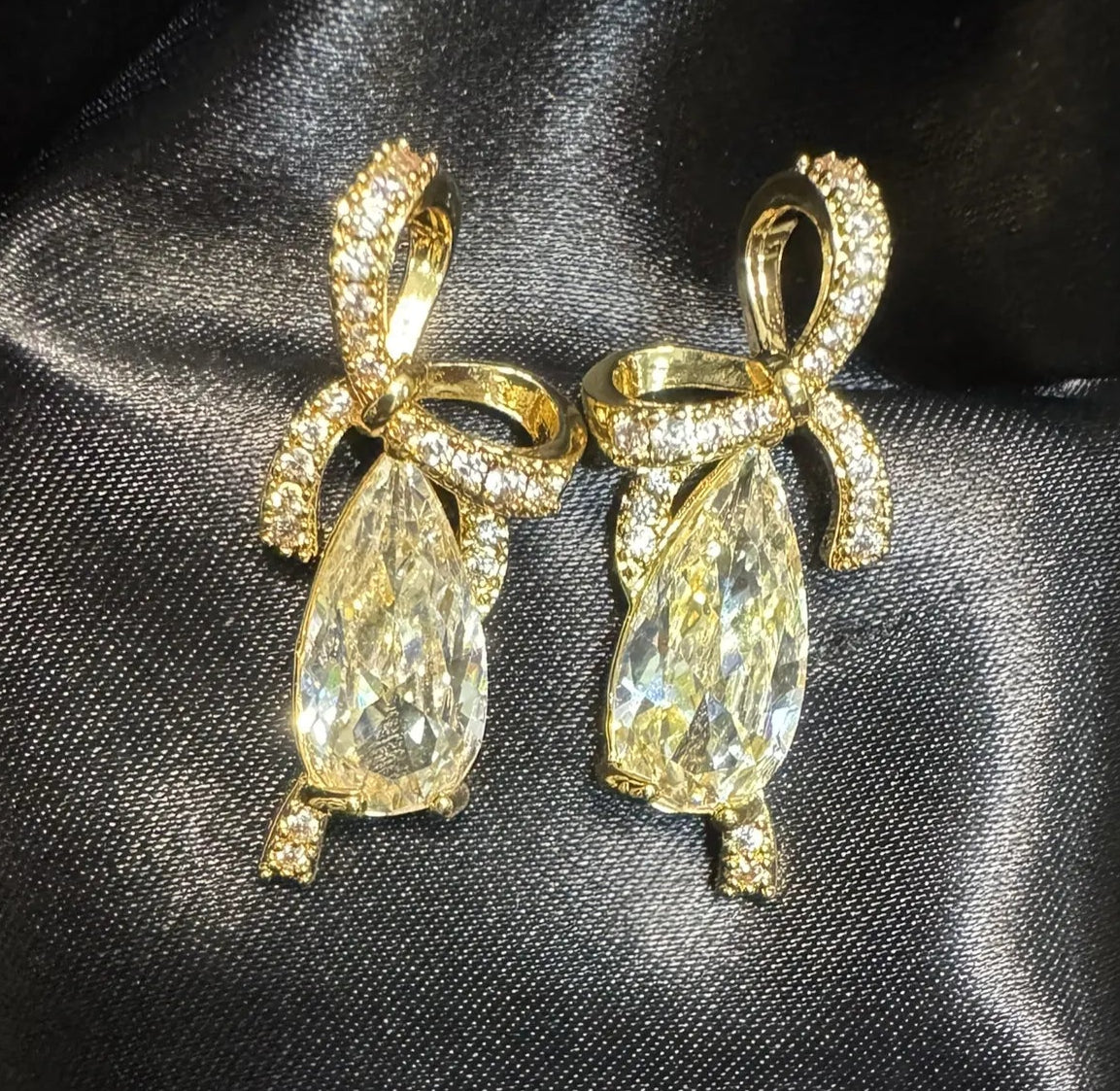 Gold earrings with large gemstones on a black satin background