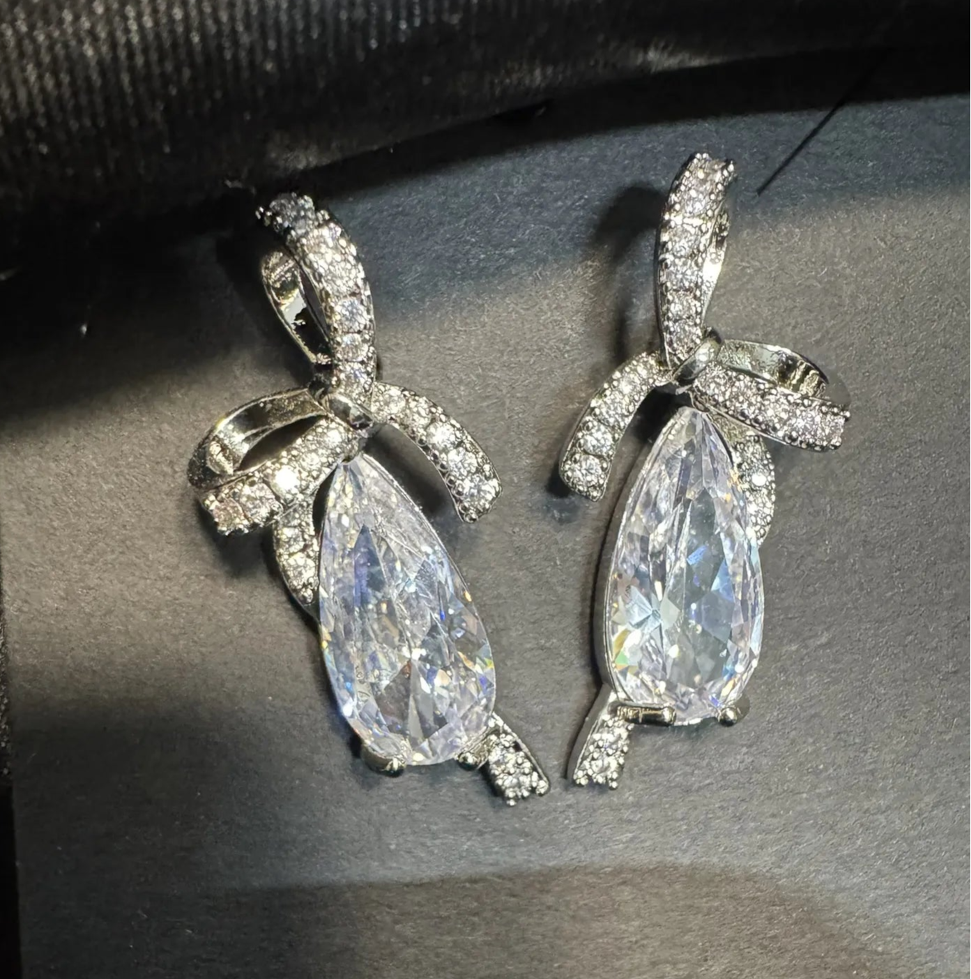 Pair of clear teardrop earrings on a dark fabric background