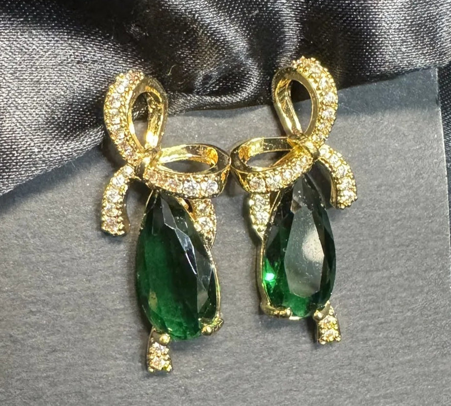 Gold earrings with green gemstones on a gray card against a black satin background