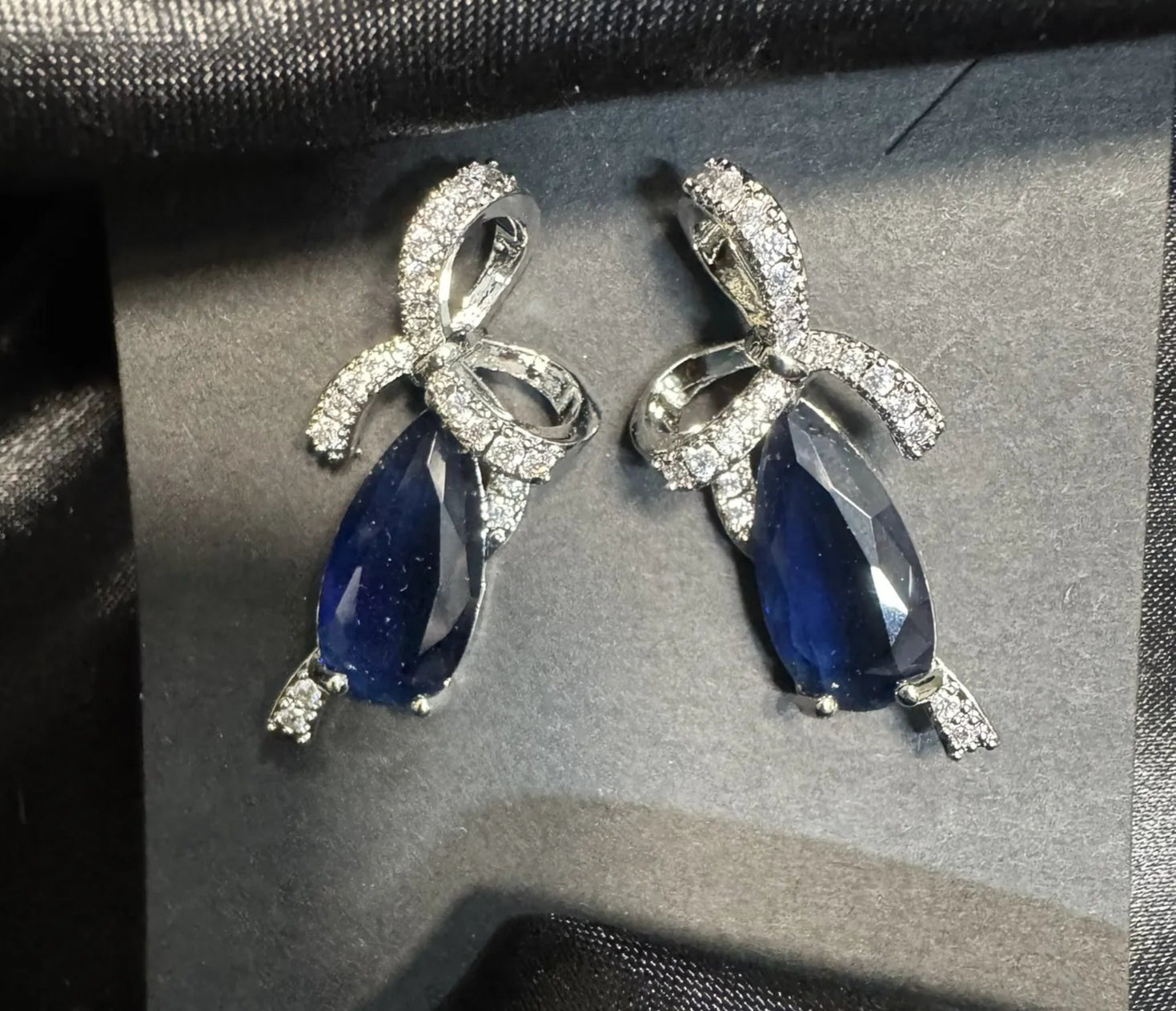 Pair of blue teardrop earrings with silver accents on a black fabric background