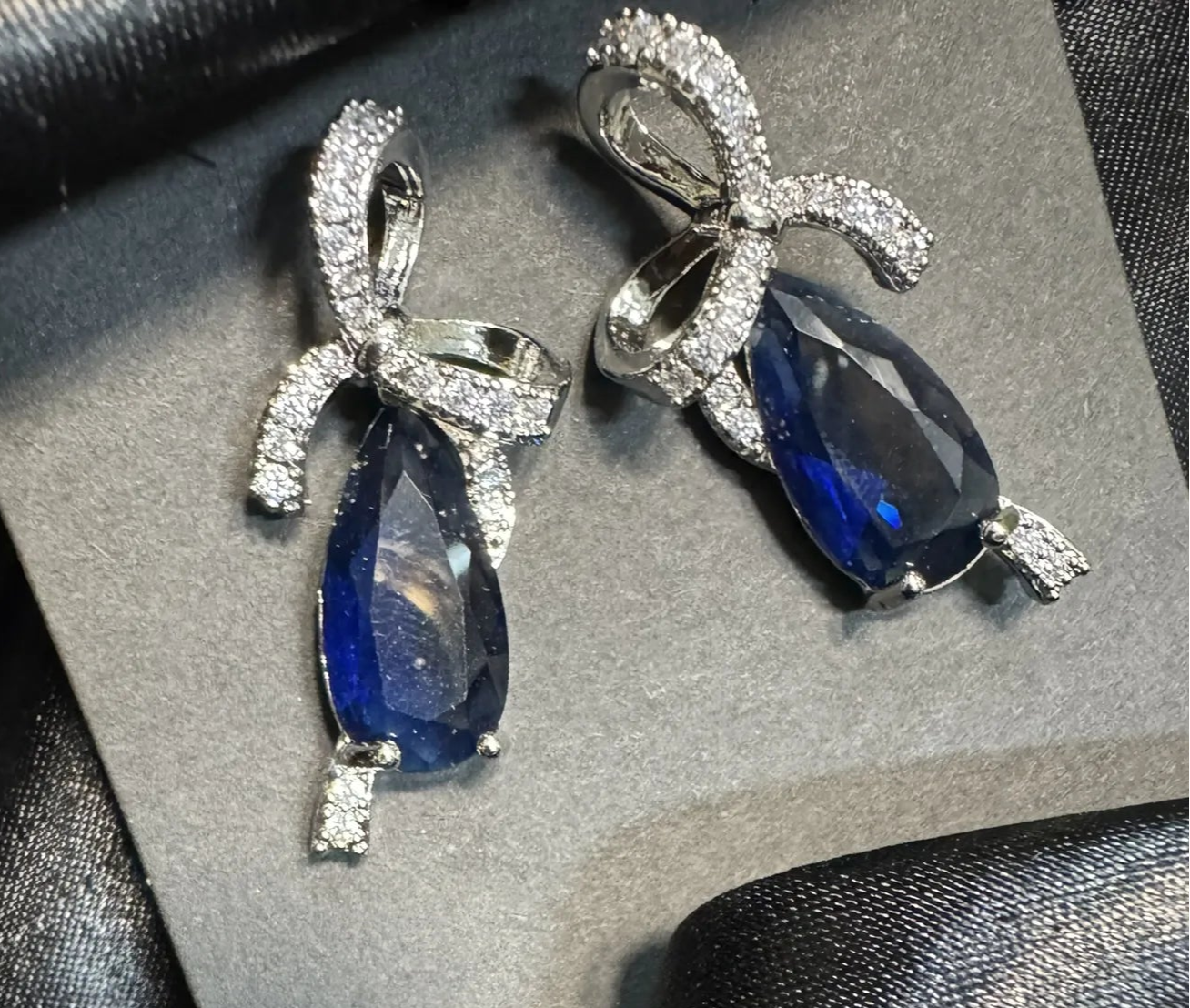Pair of earrings with blue gemstones and silver accents on a black satin surface