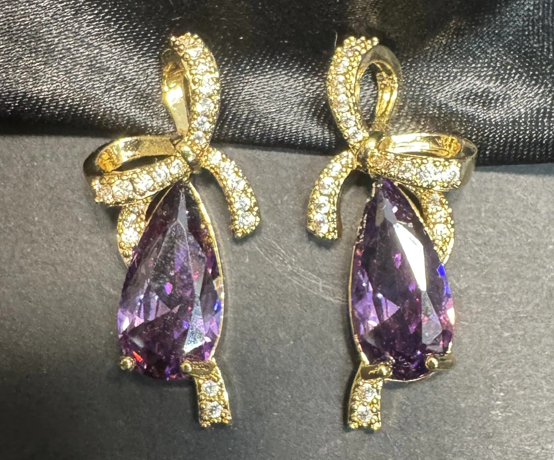 Gold earrings with purple teardrop-shaped gemstones on a dark fabric background