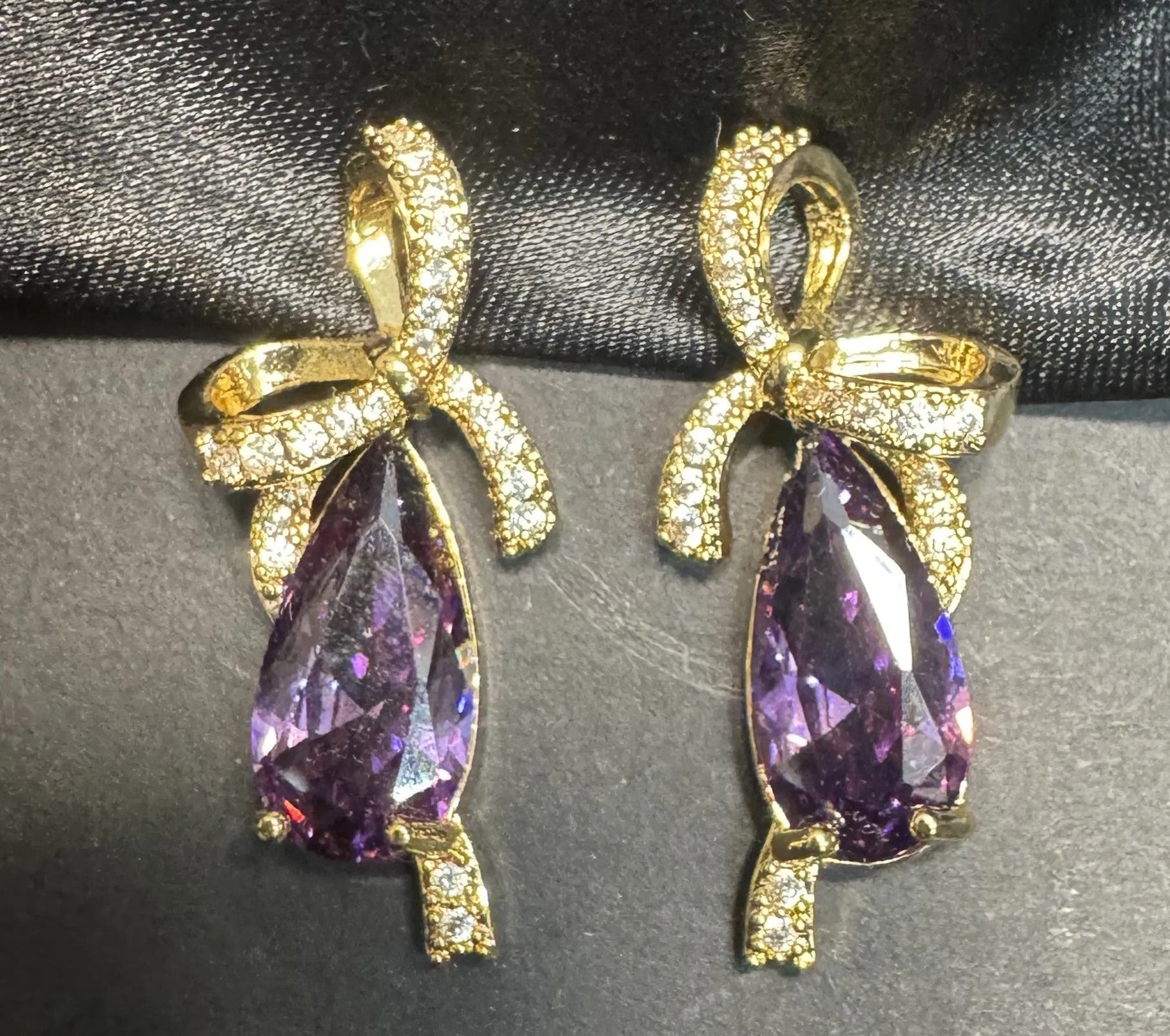 Gold earrings with purple teardrop-shaped gemstones on a dark fabric background