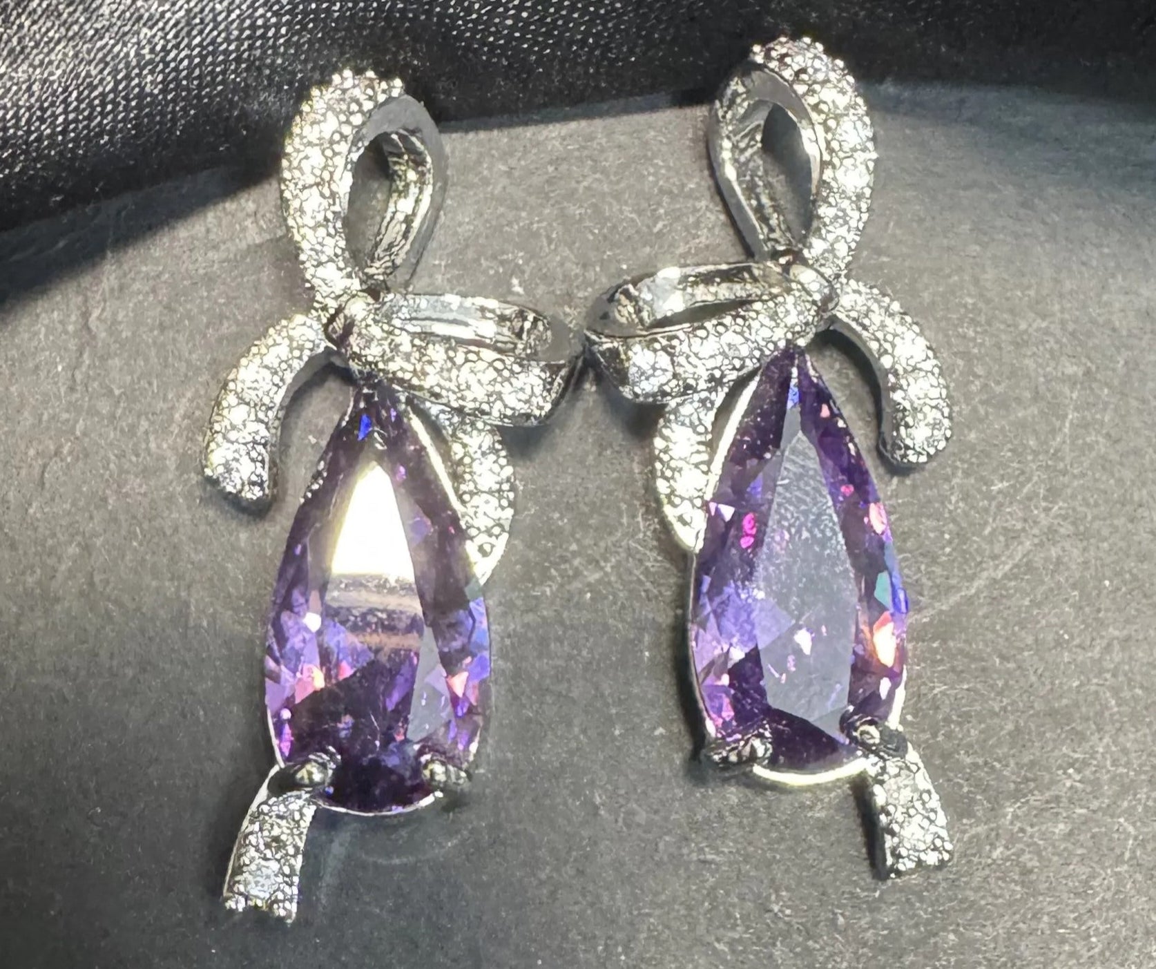 Pair of purple teardrop earrings with silver accents on a dark fabric background