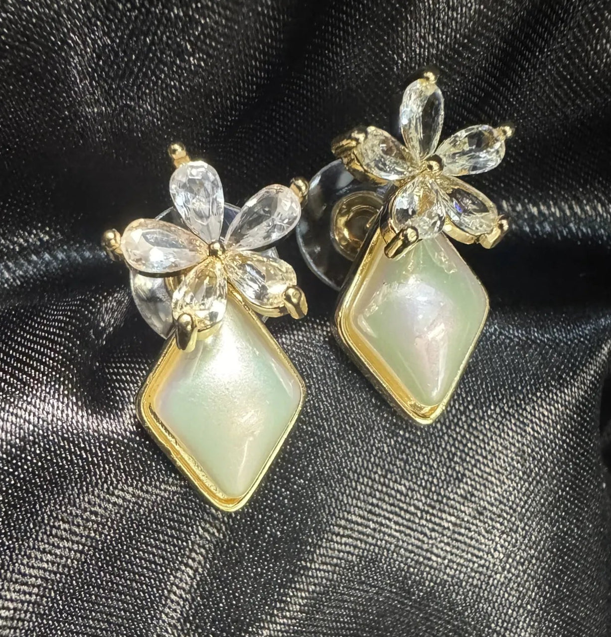 Pair of earrings with floral designs and triangular stones on a black satin background