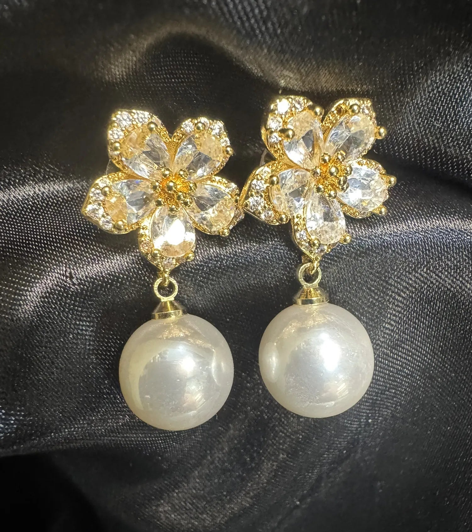 Gold floral earrings with pearl drops on a black fabric background