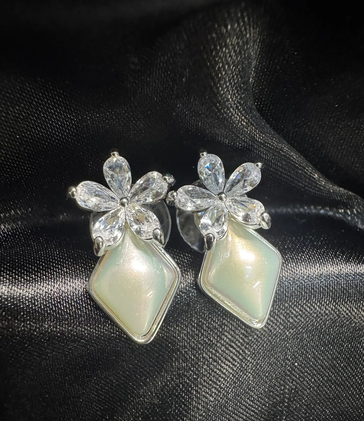 Pair of earrings with floral tops and triangular stones on a black satin background