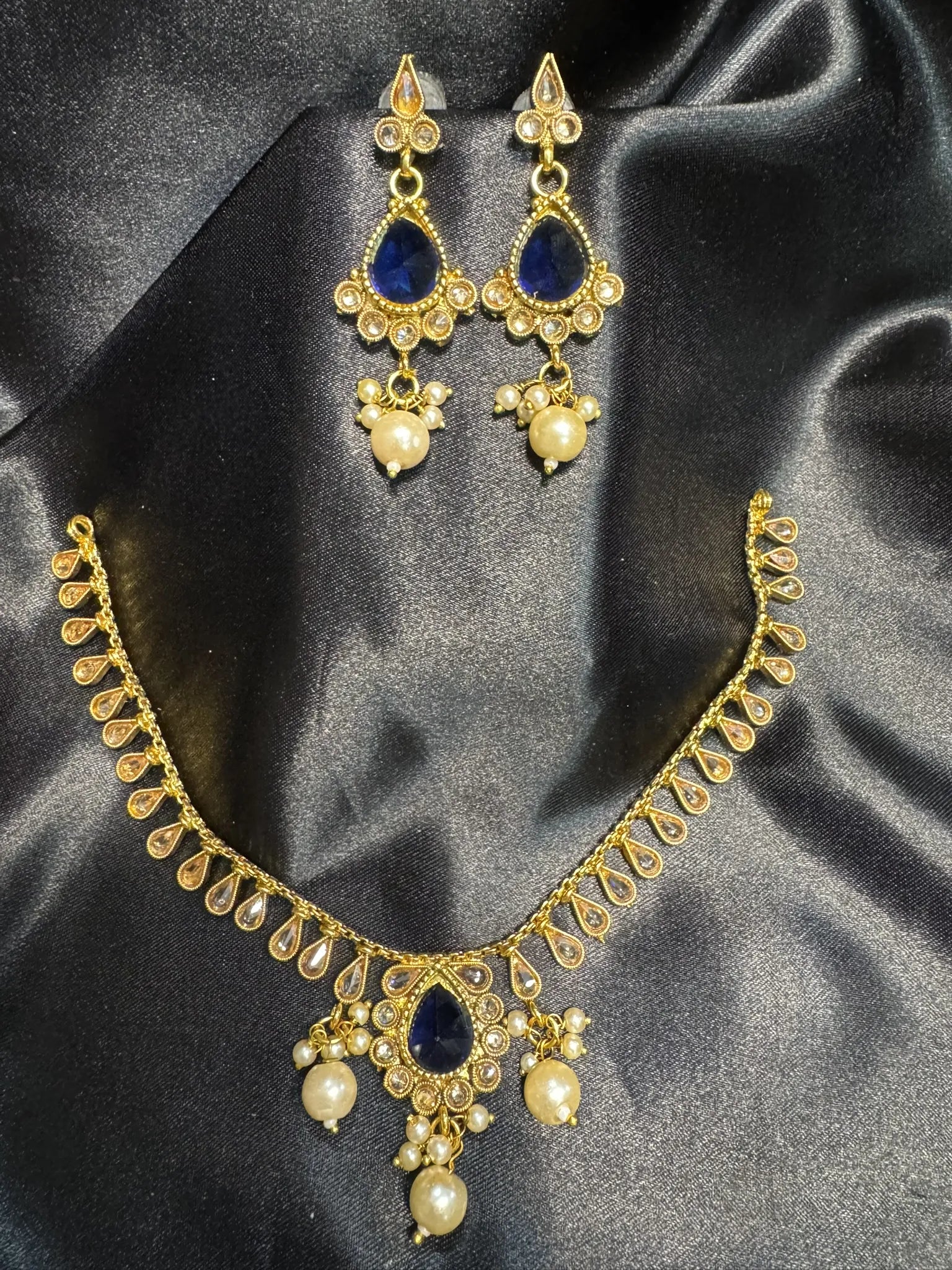 Gold necklace with blue stones and pearl-like beads on a black satin background