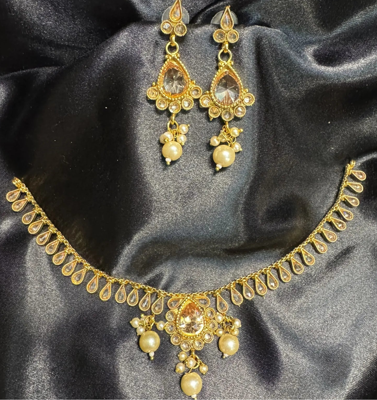 Gold necklace and earrings set on a black satin background