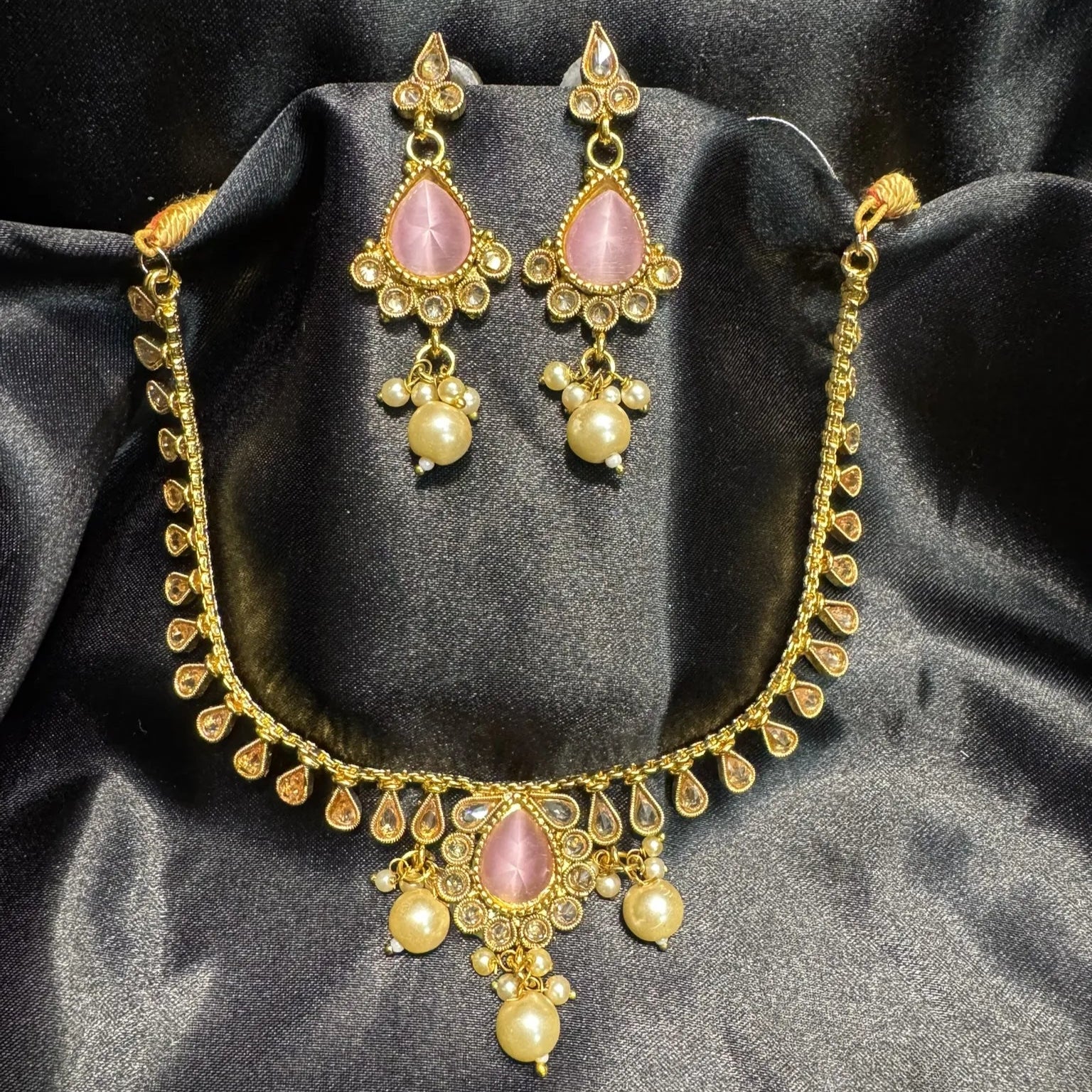 Gold necklace and earrings with pink stones on a black satin background