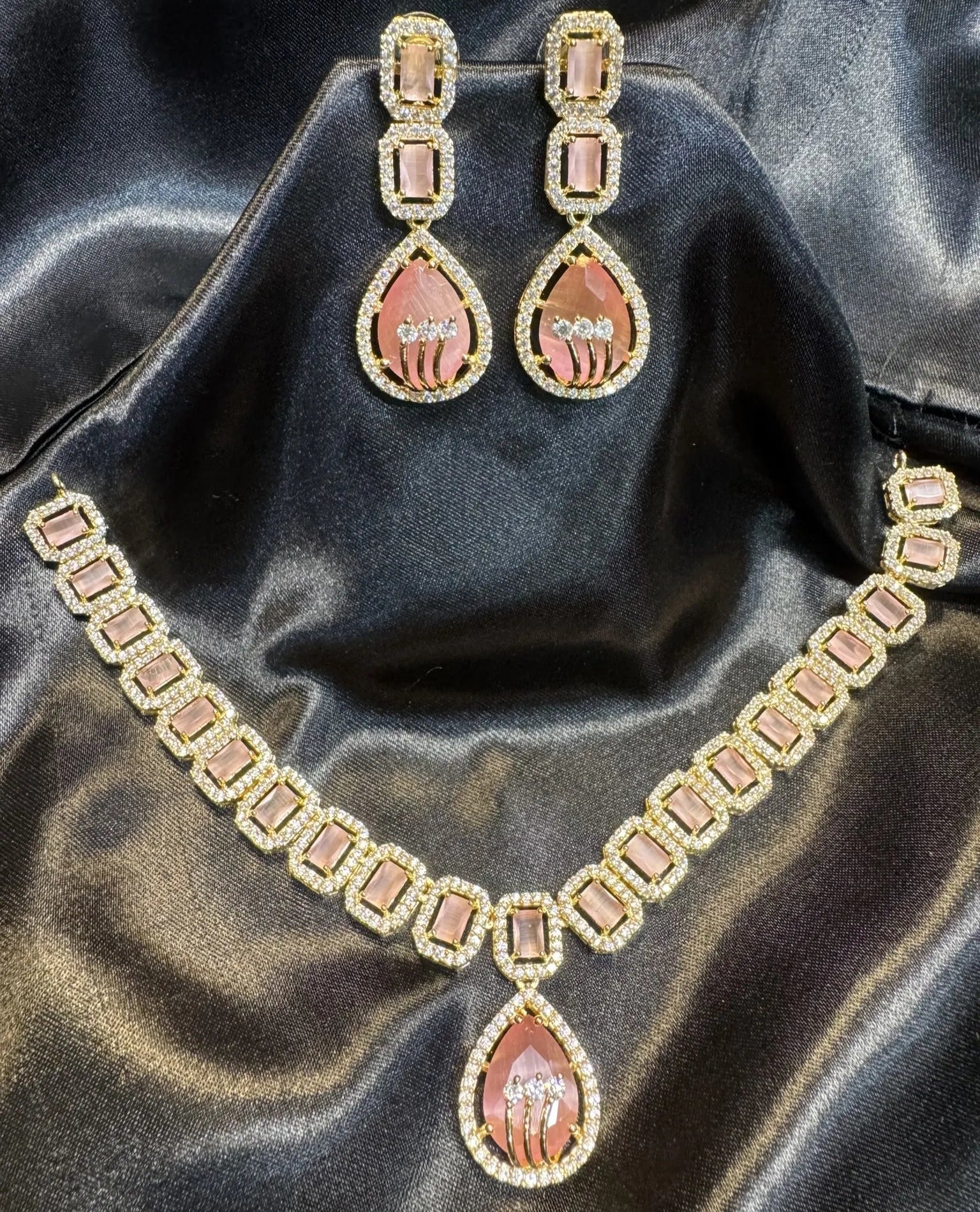 American diamond and gold plated necklace set with pink gemstones on a black satin background