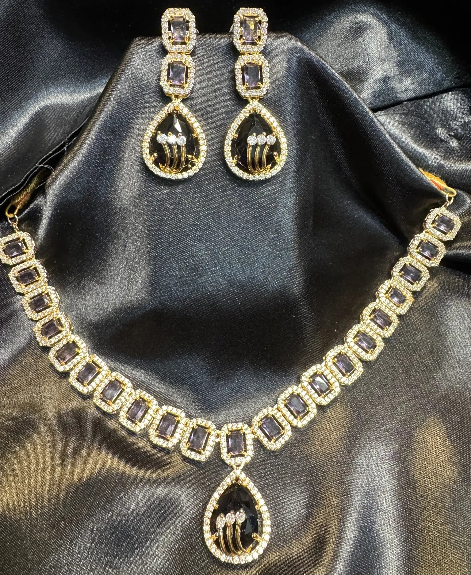American diamond and gold plated necklace set with purple gemstones on a black satin background