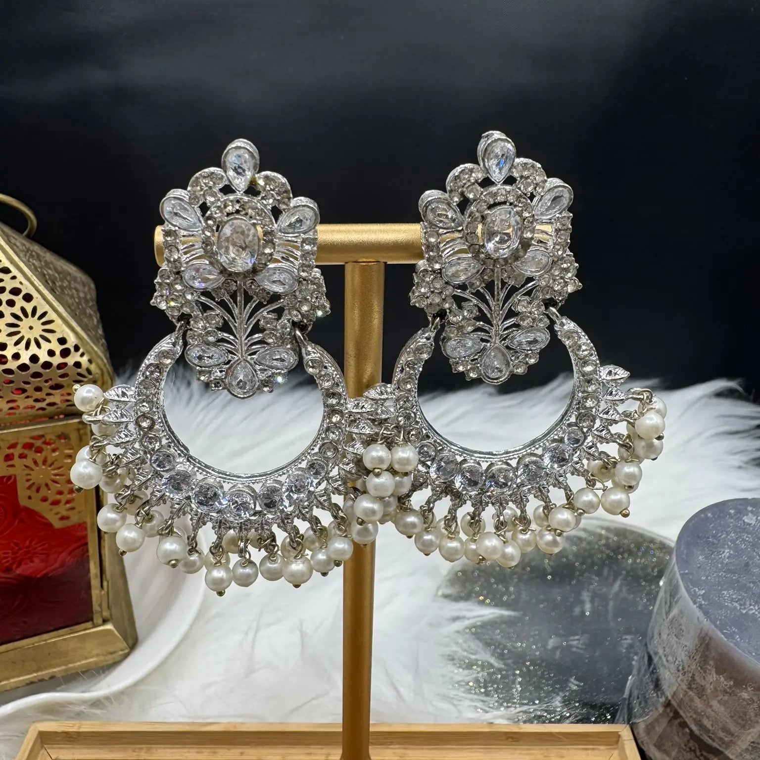Pair of ornate Pakistani style traditional silver earrings with pearls on a stand against a dark background